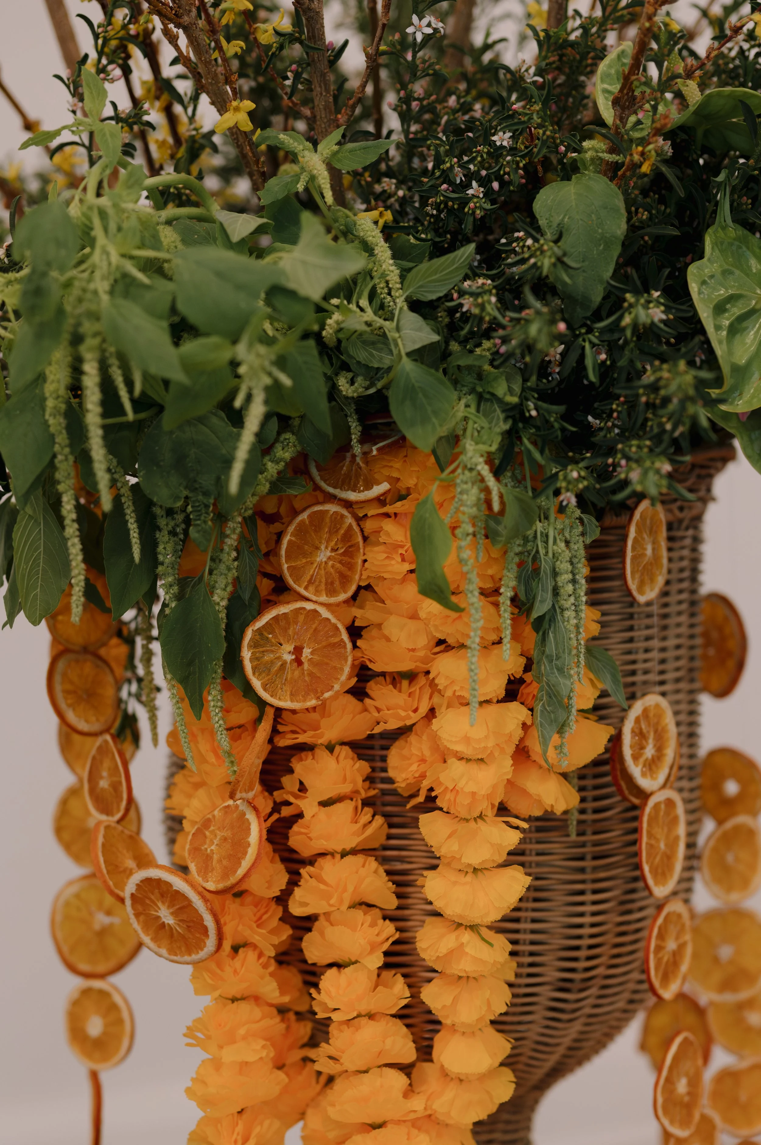 A wicker basket filled with lush green foliage, orange slices, and yellow marigold flowers.