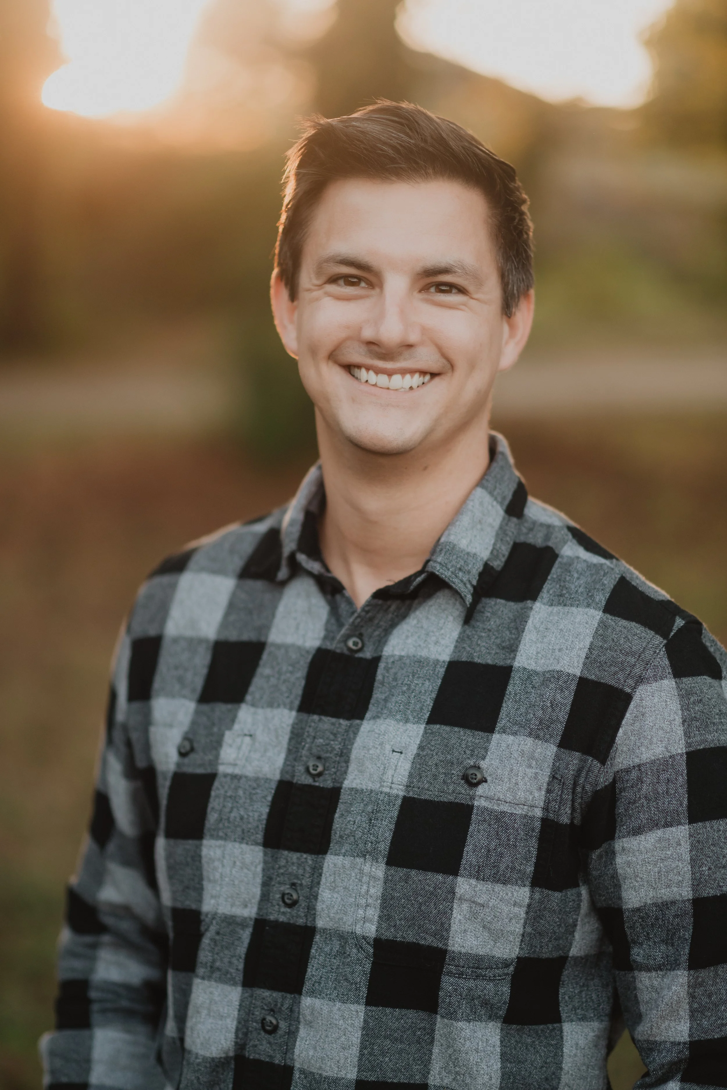 Smiling person wearing a plaid shirt outdoors.
