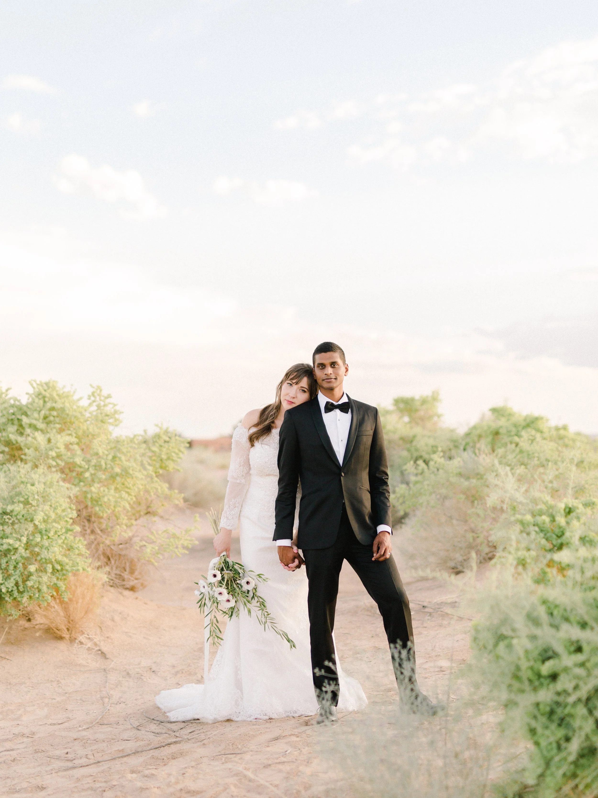 Bride and groom hold hands side by side while bride rests her head on grooms shoulder in a desert landscape. #danielleelizabethweddings #destinationweddingphotography #destinationweddingvideography #oklahomaluxuryphotographer