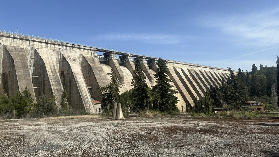 Una presa de agua de gran tamaño con varias compuertas, rodeada de árboles y un cielo despejado.