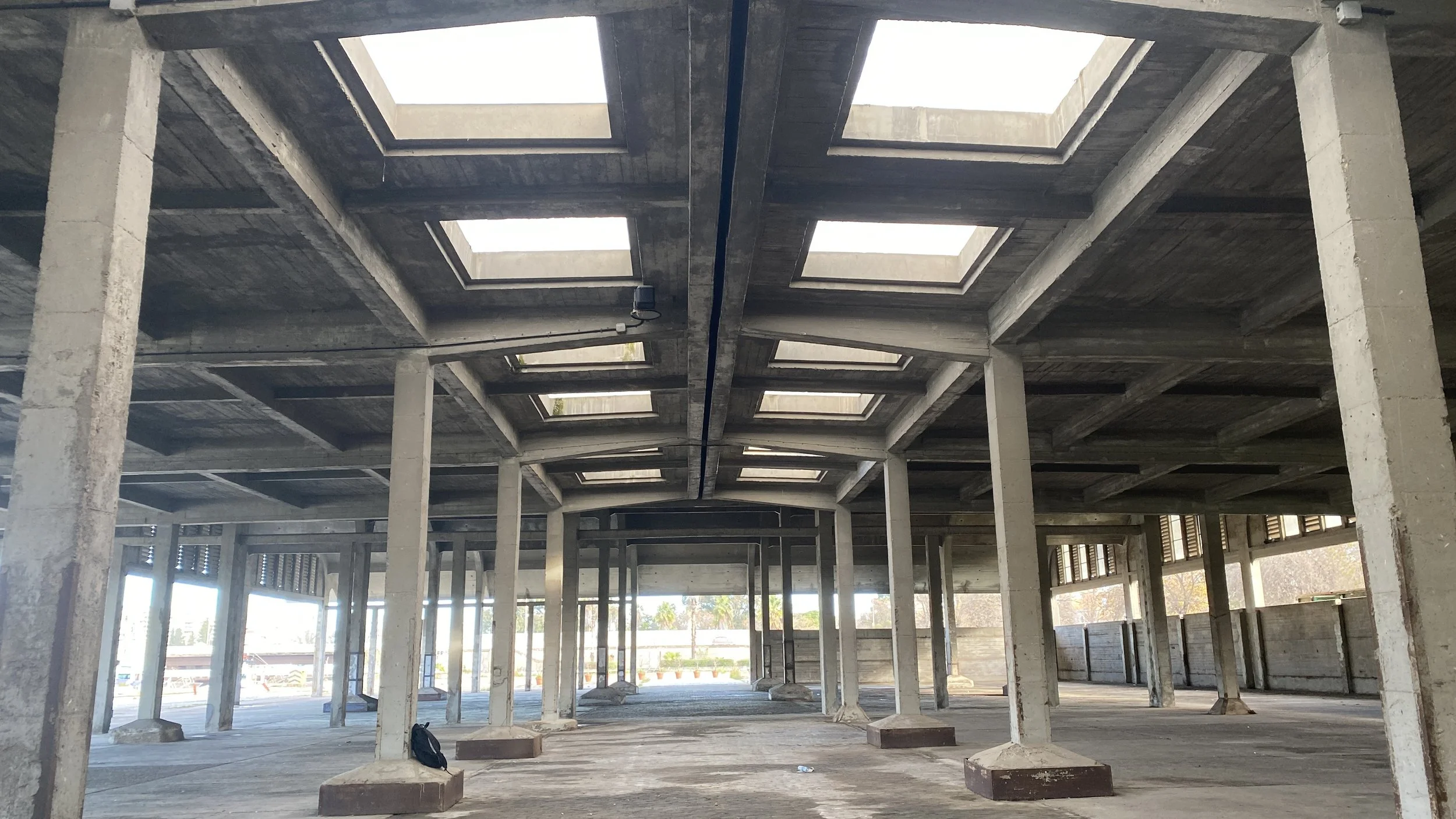Estructura de concreto en construcción con almenas en el techo y pilares, luz natural entrando por ventanas abiertas.