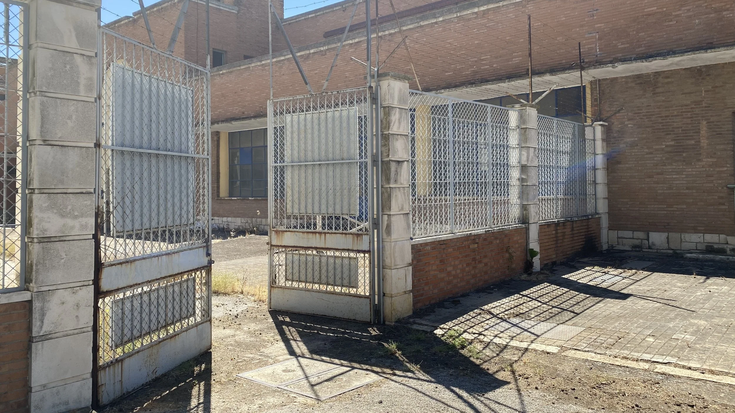 Entrada con rejas de metal, muro de ladrillos y ventanas en un edificio en construcción o en estado de abandono