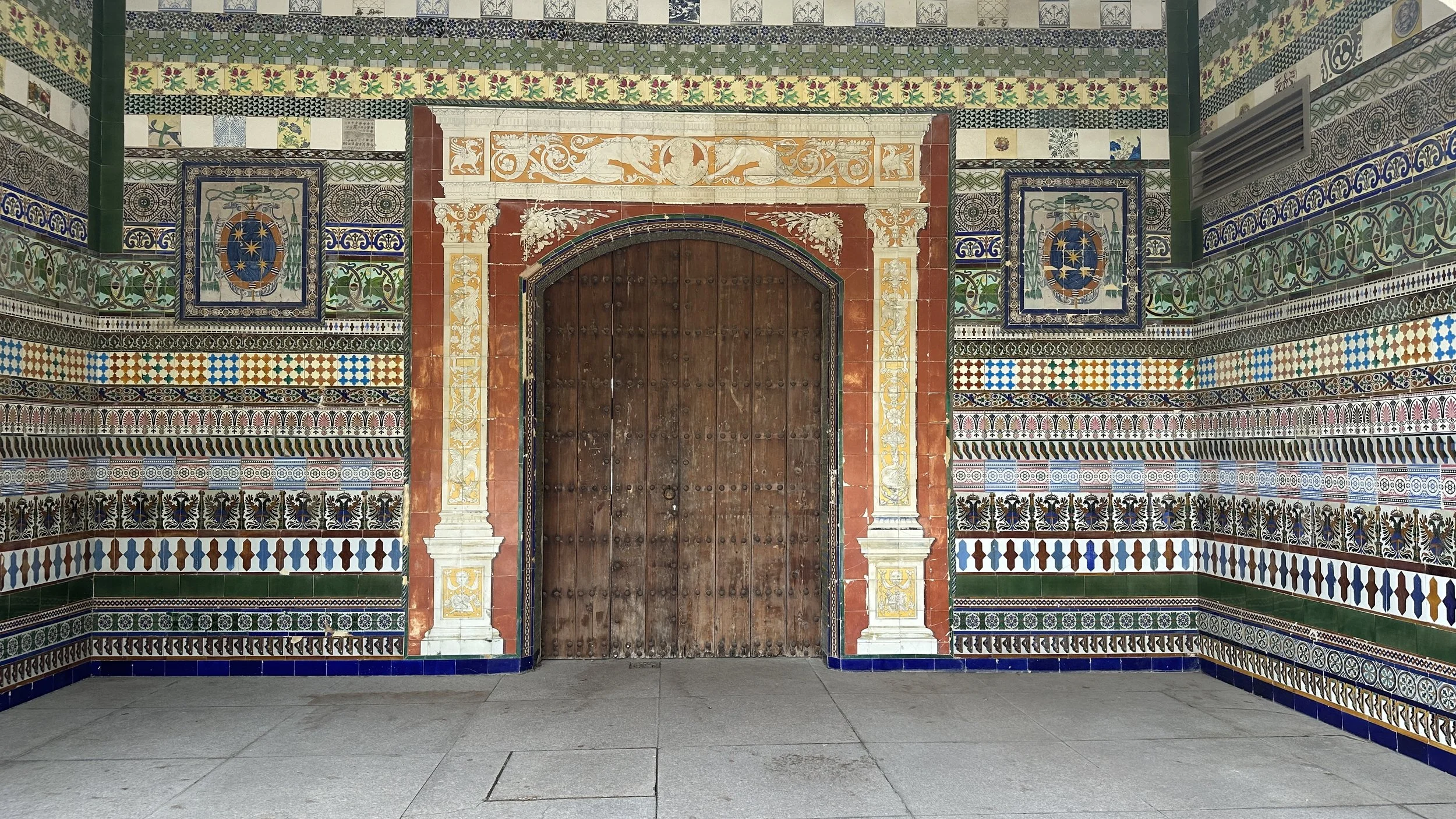 Puerta de madera rodeada de azulejos coloridos y decorativos en un estilo andaluz, con detalles en blanco, azul, verde y naranja.