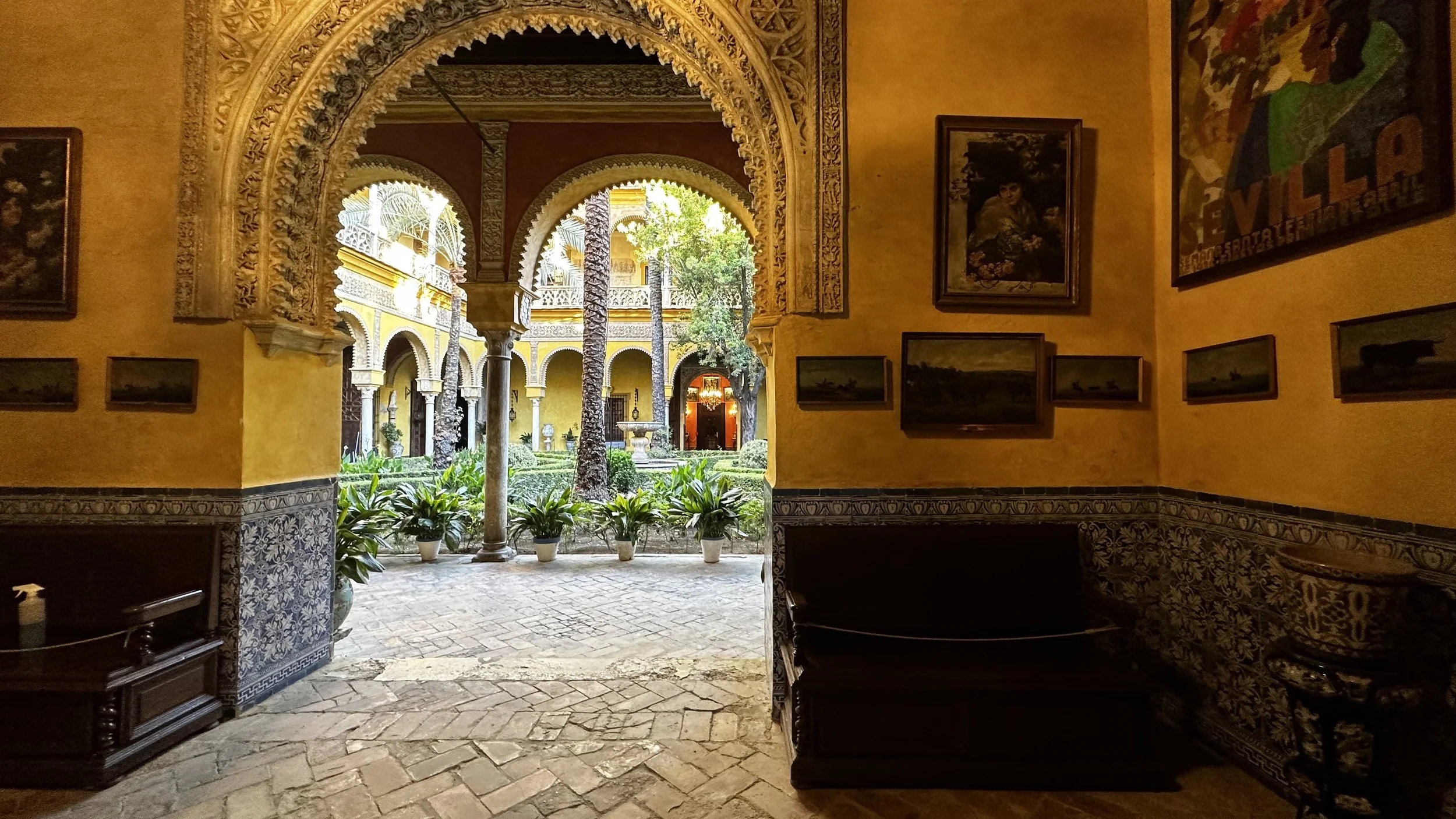 Vista de un patio interior de estilo colonial con arcos decorativos, plantas en macetas y un ambiente luminoso.