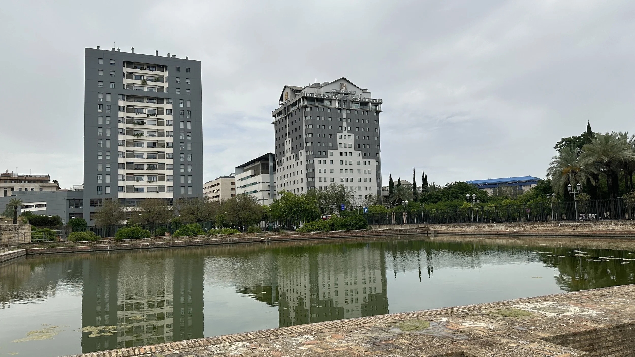 Dos edificios altos y modernos al lado de un canal con vegetación y árboles