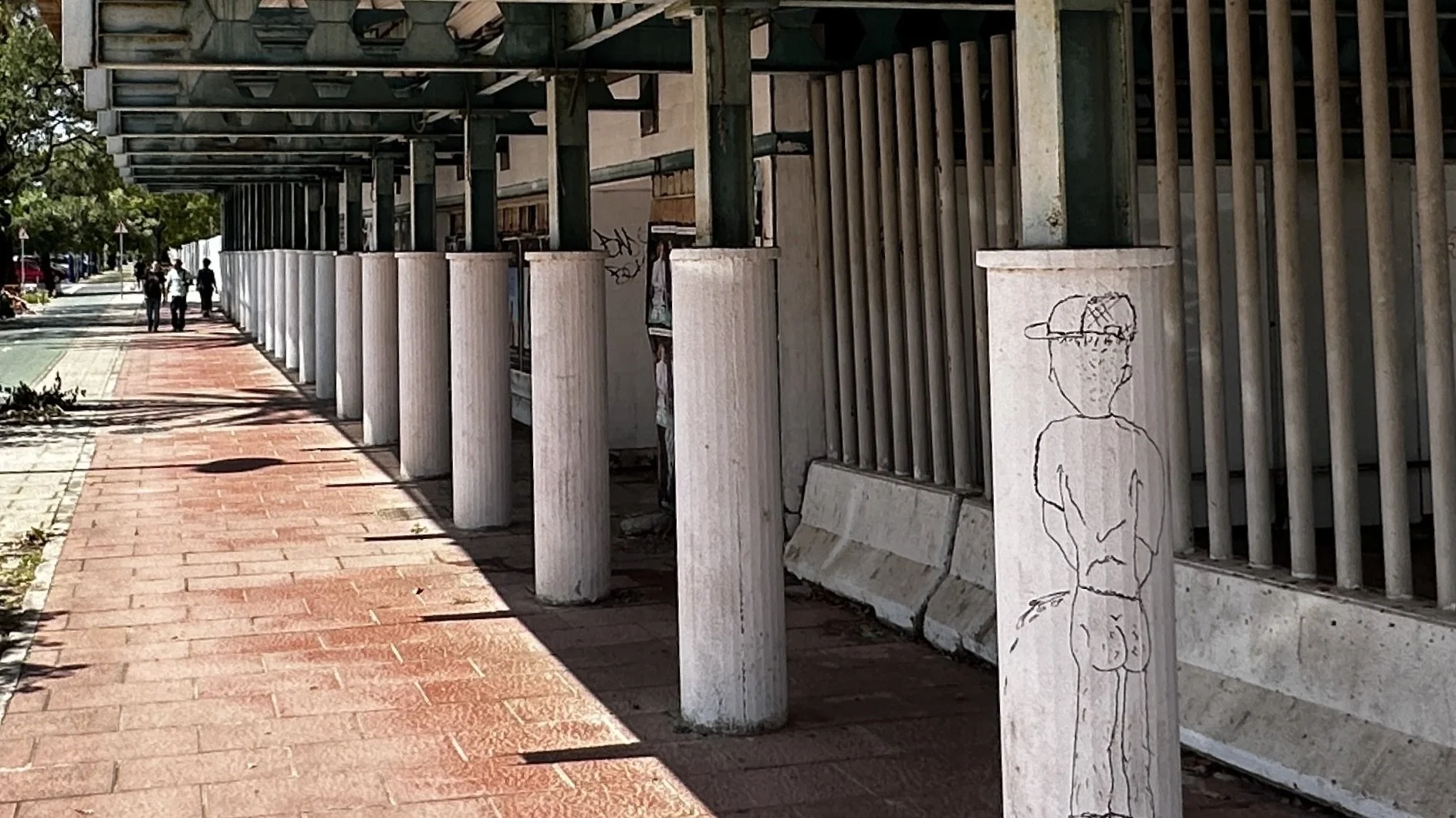 Línea de columnas blancas en la acera con un mural de un dibujo de un niño con gorra.