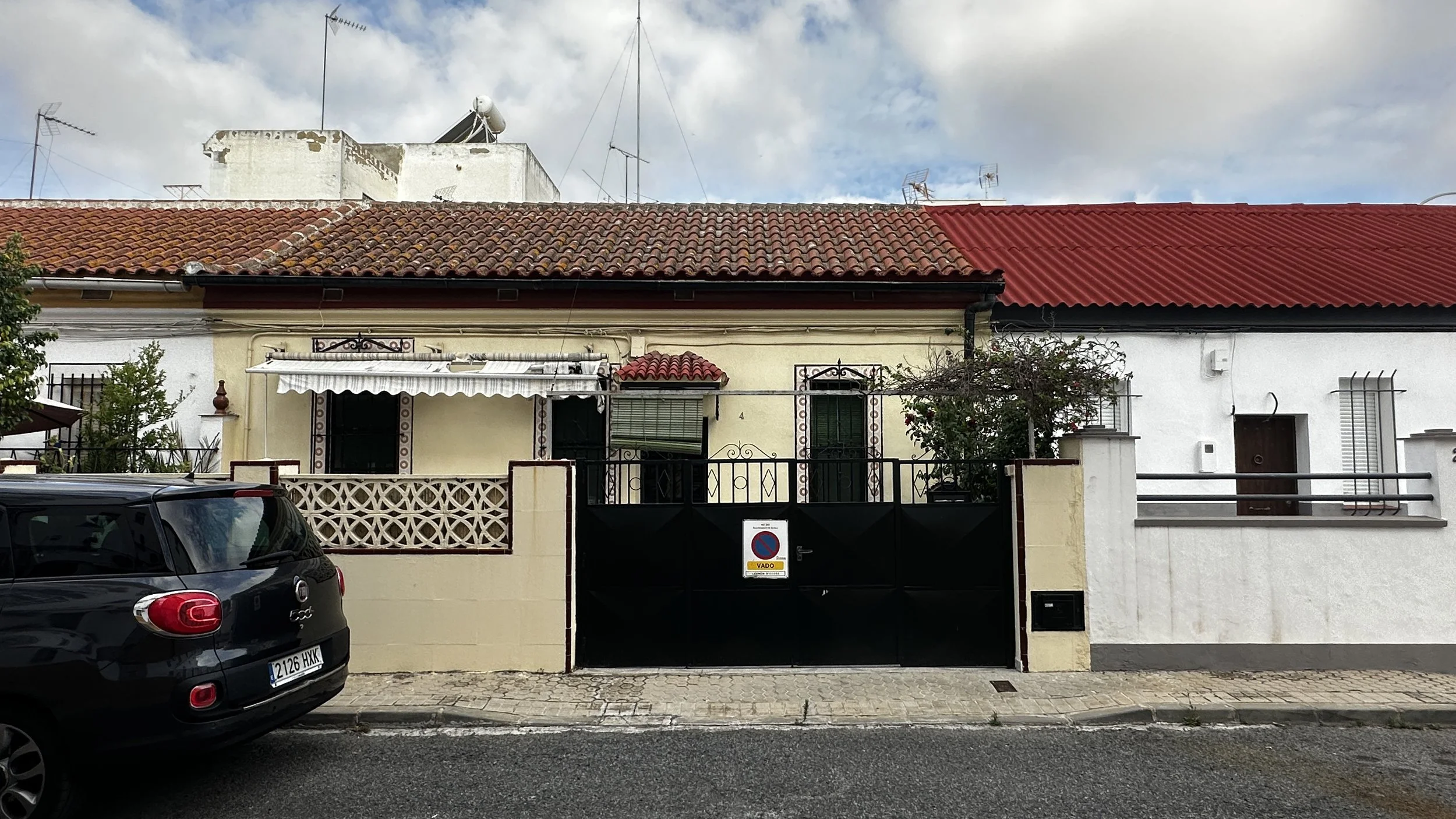 Casas residenciales con techos de tejas y jardineras, un automóvil negro en la calle y un cartel de 'prohibido estacionar'.