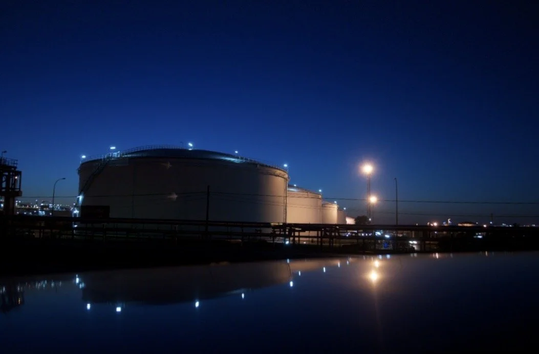 Tanques de almacenamiento de petróleo con luces nocturnas y reflejo en el agua
