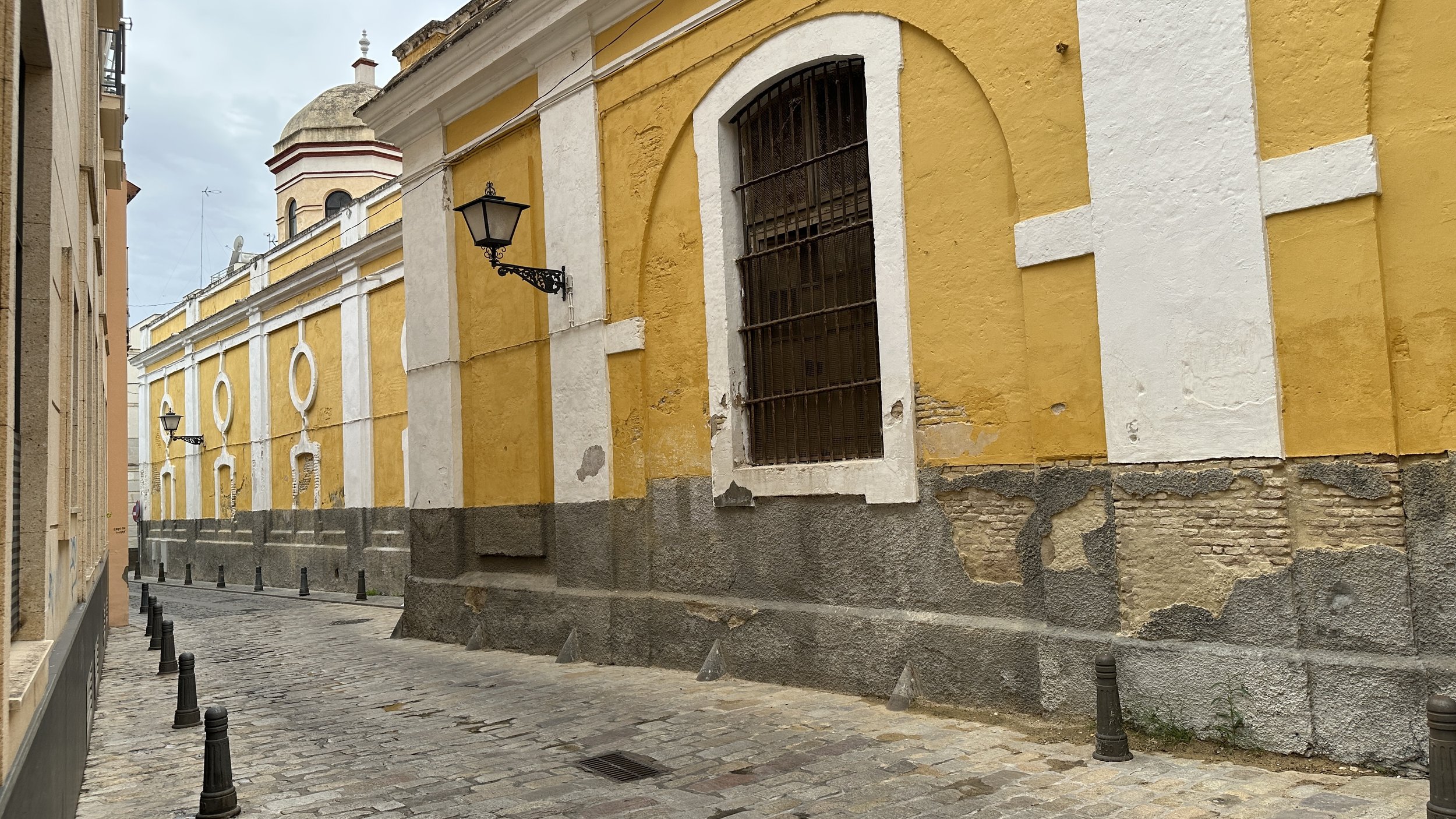 Calles empedradas en un barrio antiguo con fachadas amarillas y ventanas con rejas, faroles de hierro en la pared, en un día nublado.