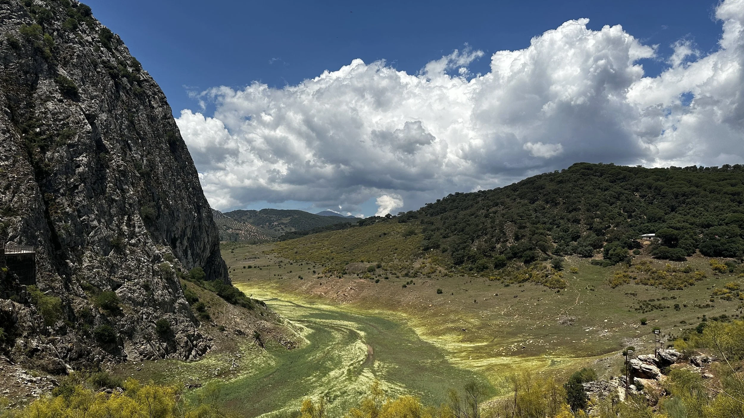 Paisaje de montañas con un valle y un río con vegetación, cielo con nubes