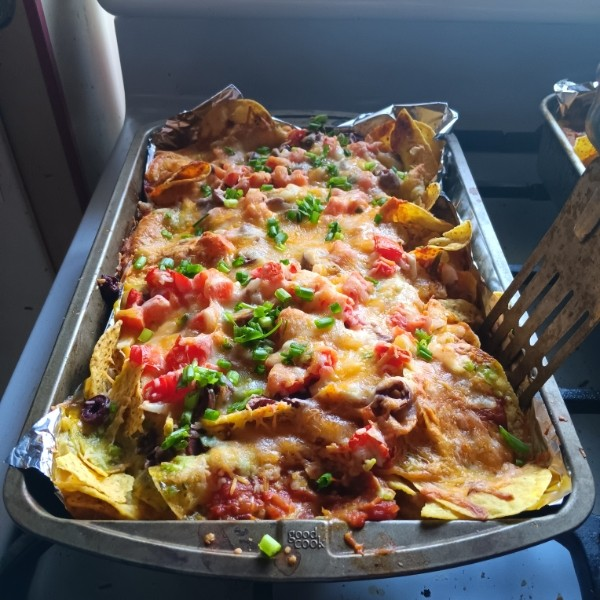 Baked nachos with melted cheese, chopped tomatoes, green onions, and beef on a metal baking sheet