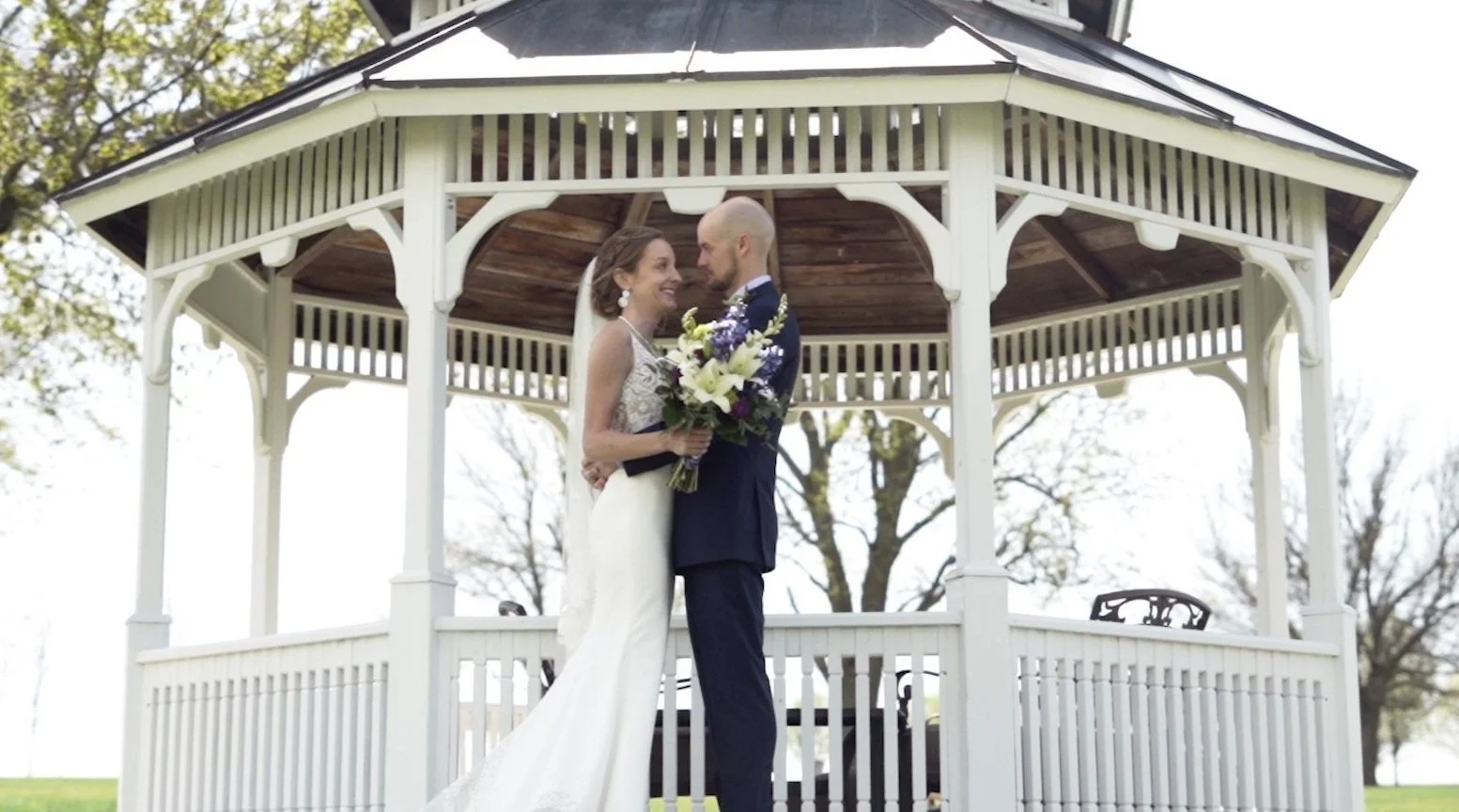 bride and groom smiling at each other in front of a pergola