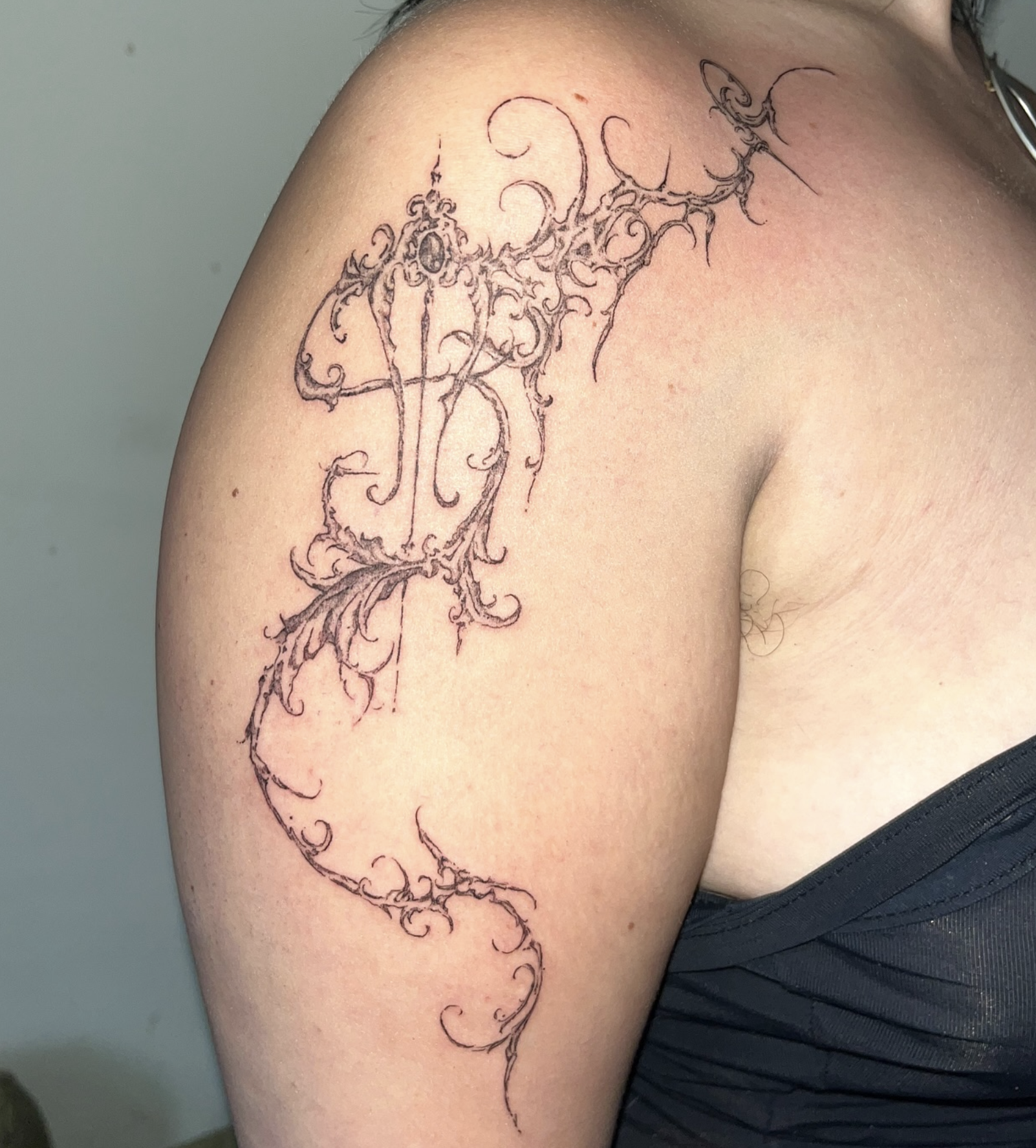 Schwarz-weiß Tatzentattoo am Schulterblatt einer Person, mit vielen feinen Linien und details, auf dunkler Kleidung.
