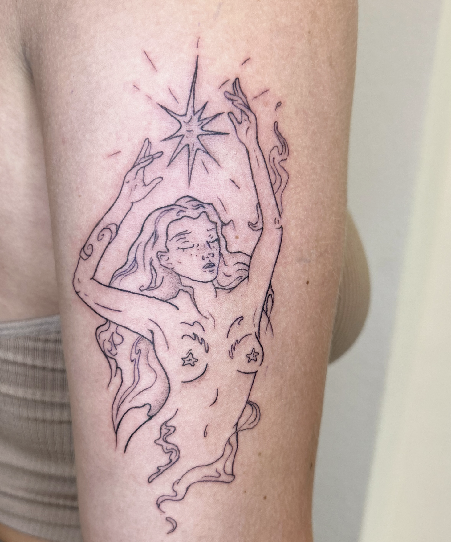 Tattoo eines weiblichen Mädchens mit langen, fließenden Haaren und einer schimmernden Sternenspur, blassem Gesicht, geschlossenen Augen und lächelnden Lippen.