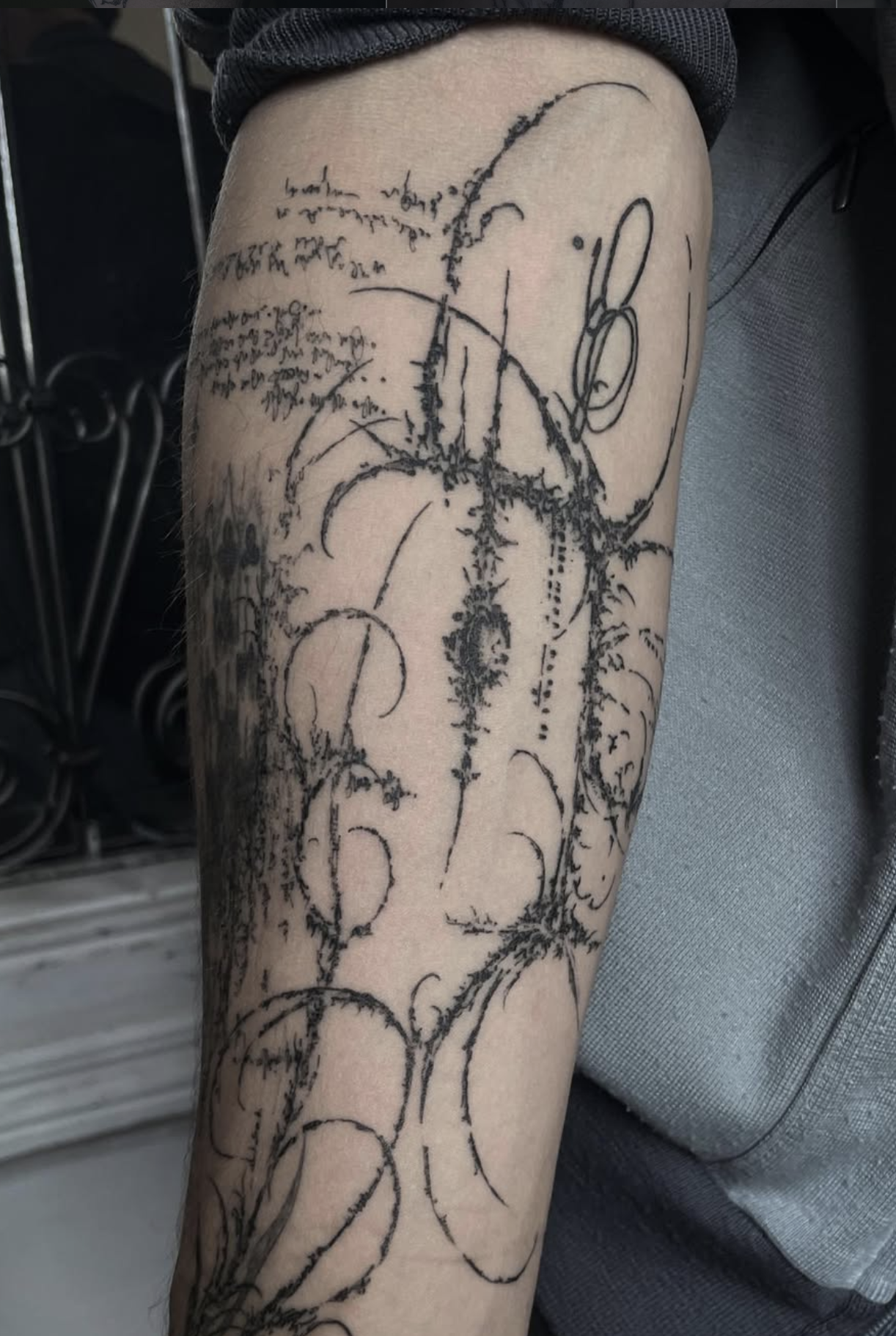 Schwarz-weiße Tätowierung auf dem Oberarm, bestehend aus kalligrafischen Linien, geometrischen Formen und handgeschriebenem Text.