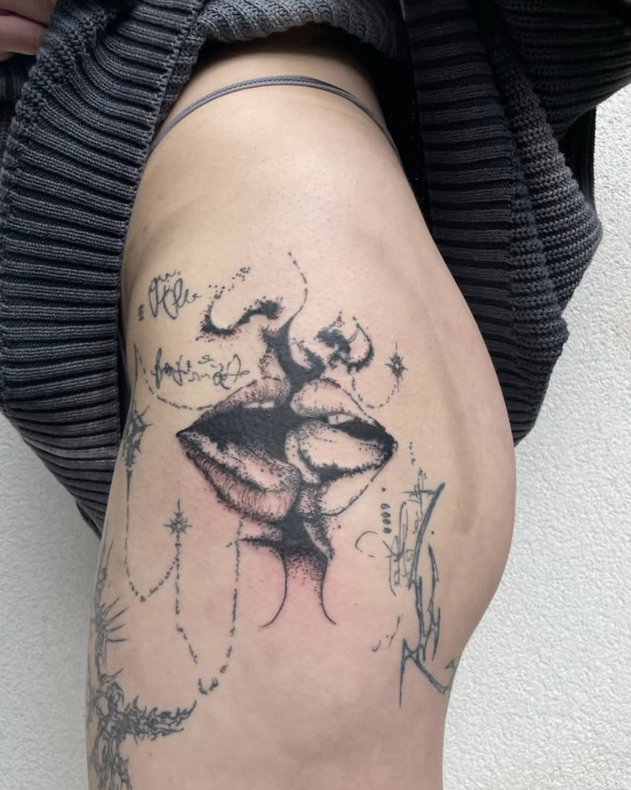 Tattoo eines Gesichts mit geschlossenen Augen und Lippen, mit mehreren kleinen Sternen, Linien und Texten umgeben.