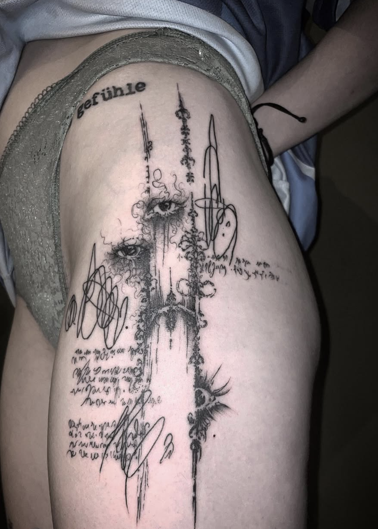 Tattoo auf Oberschenkel mit der deutschen Übersetzung "BeFÜhle" und einer künstlerischen Skizze eines Auges sowie handgeschriebener Notizen.