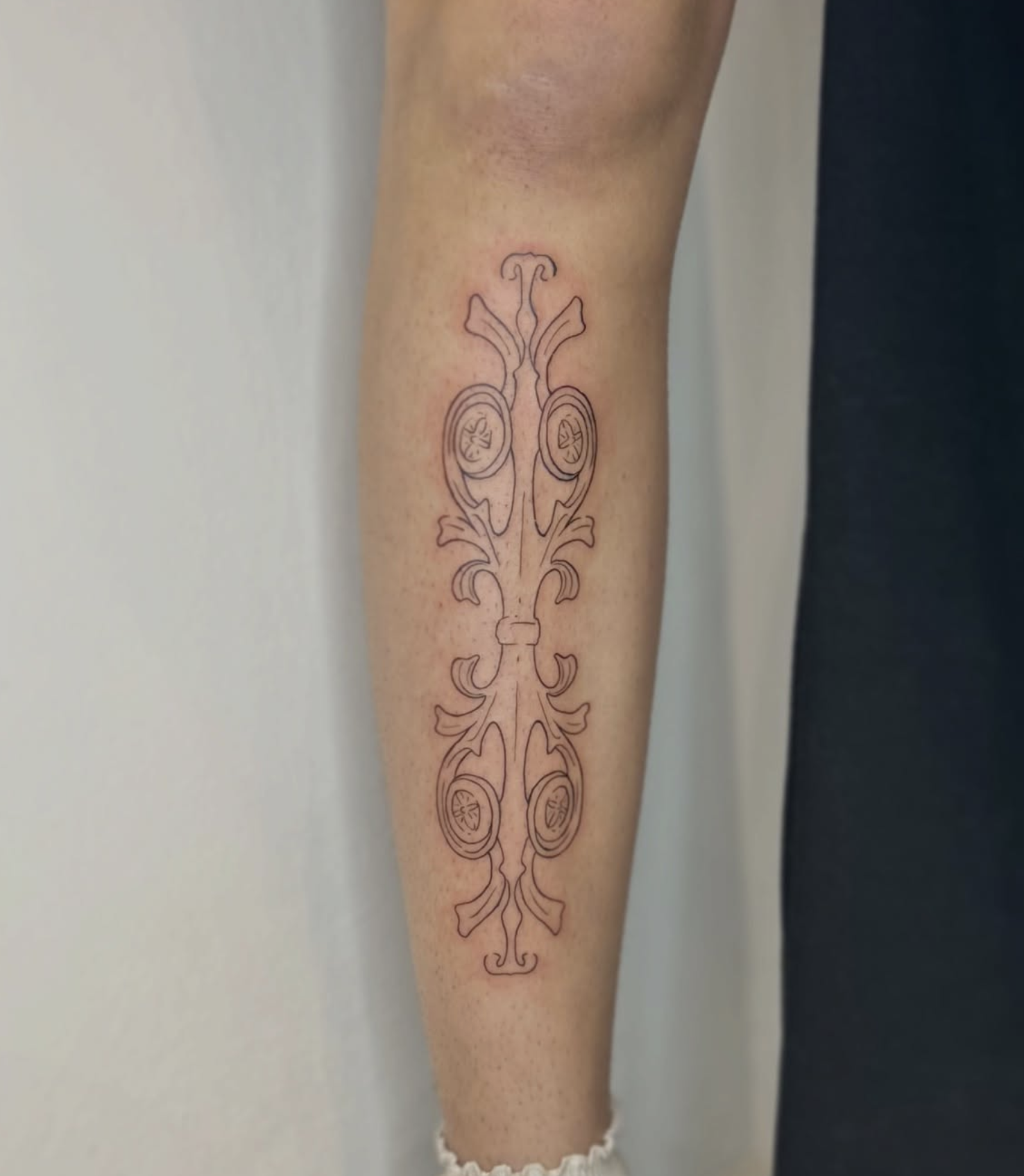 Linienförmiger Tattoo-Entwurf auf dem Unterarm, der symmetrische, dekorative Muster und kegelförmige Elemente zeigt.