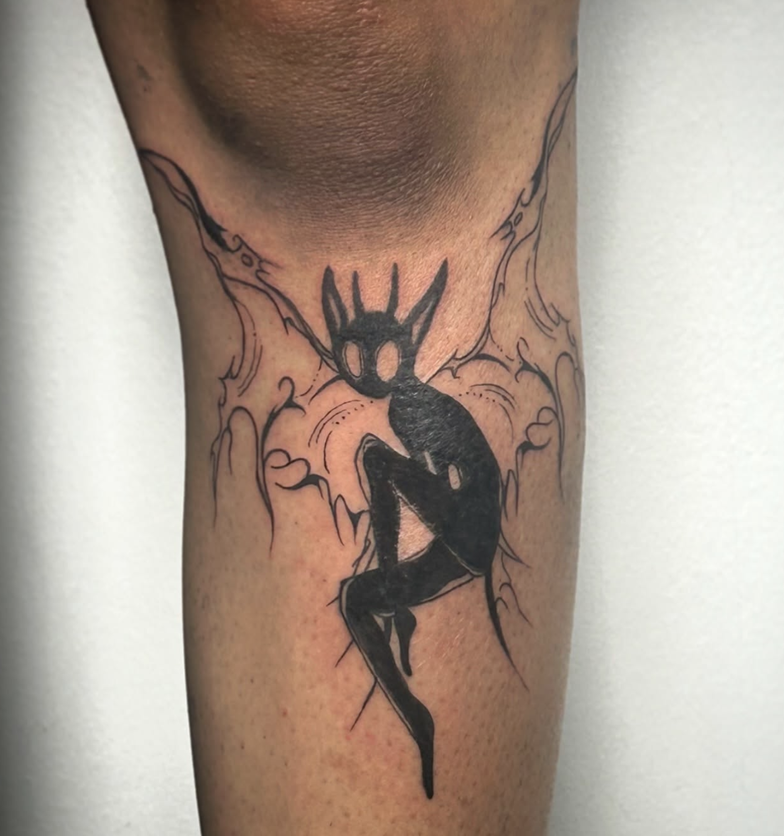 Tattoo eines dunklen Wesens mit große Ohren und langen Haaren auf dem Oberschenkel.