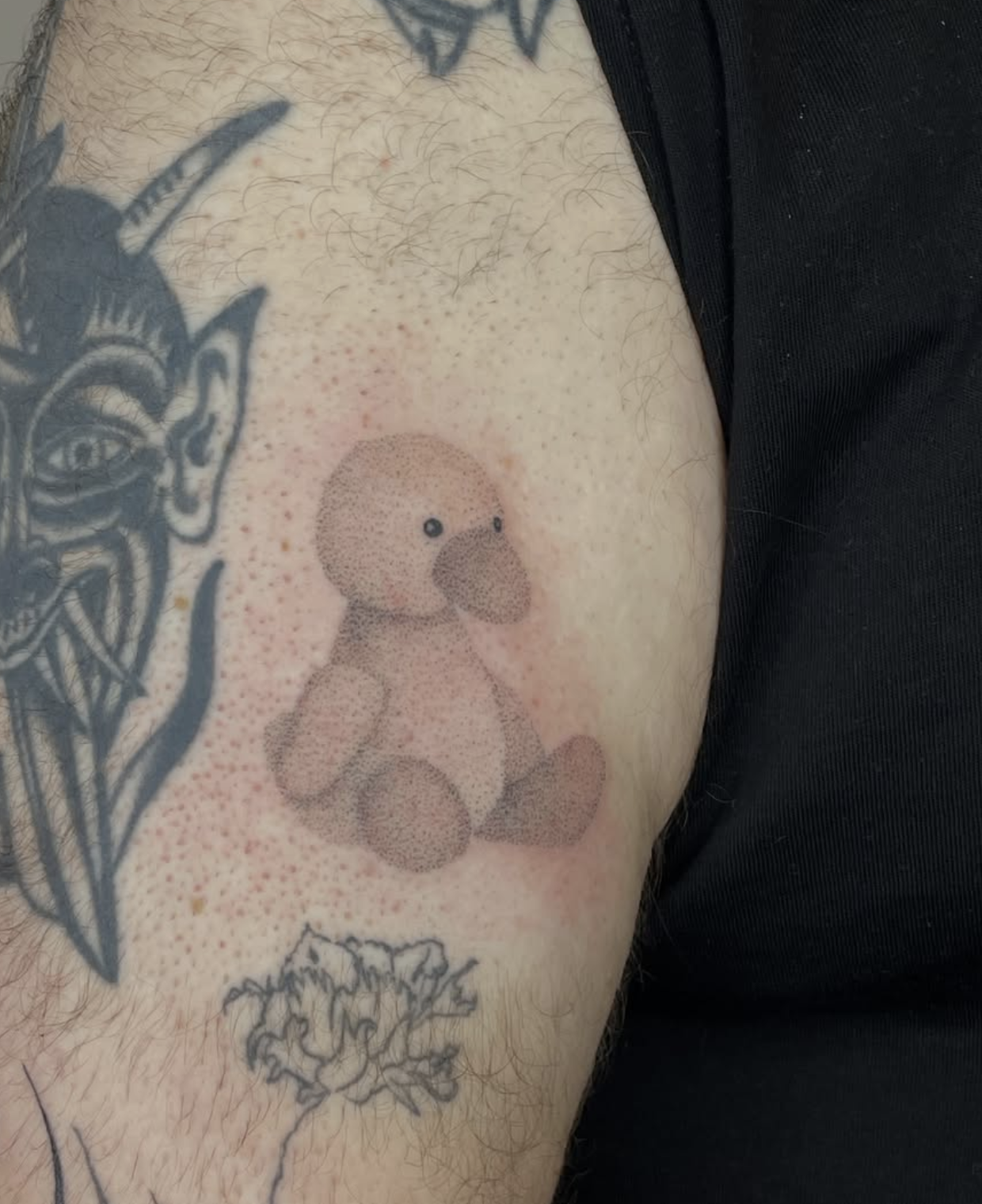 Tattoo eines Teddybären auf Haut mit mehreren anderen Tätowierungen im Hintergrund.