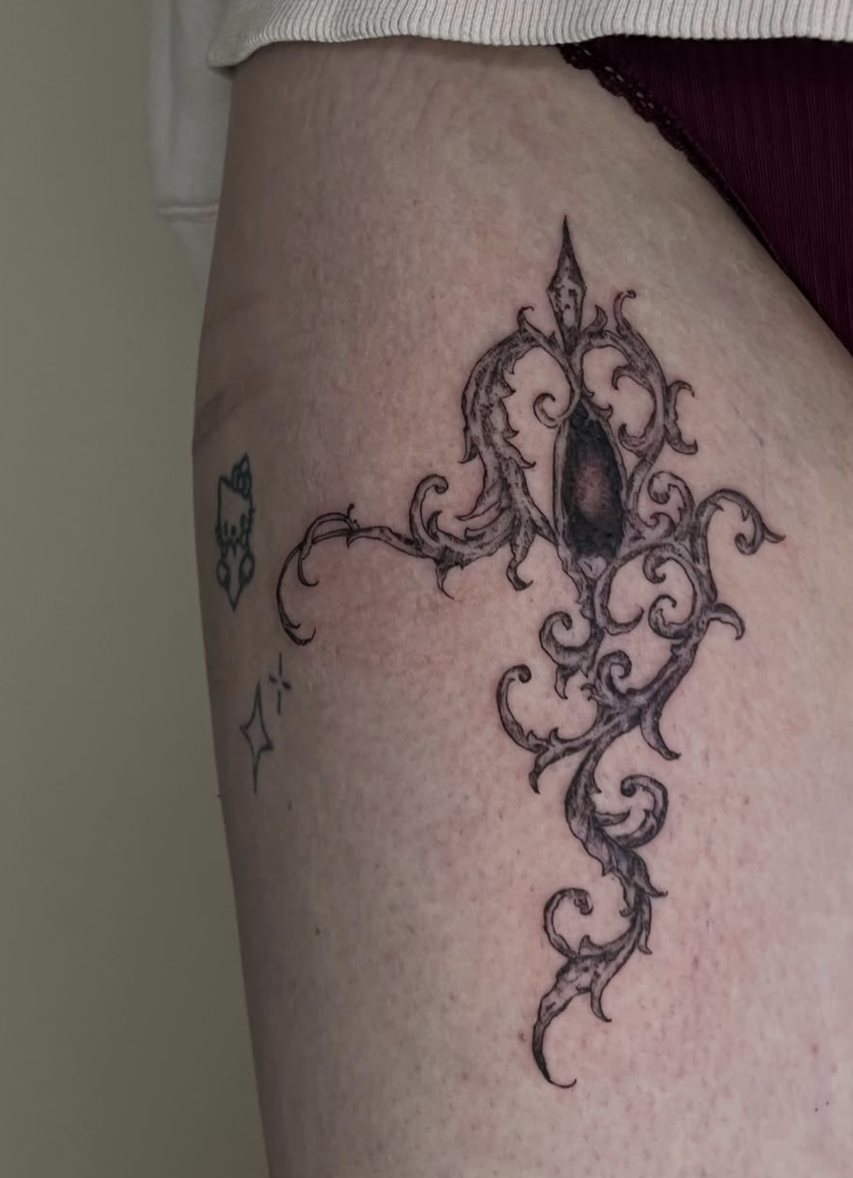 Tattoo eines mystischen, geschwungenen Designs auf der Haut, ergänzt durch kleine Stern- und Herzsymbole.