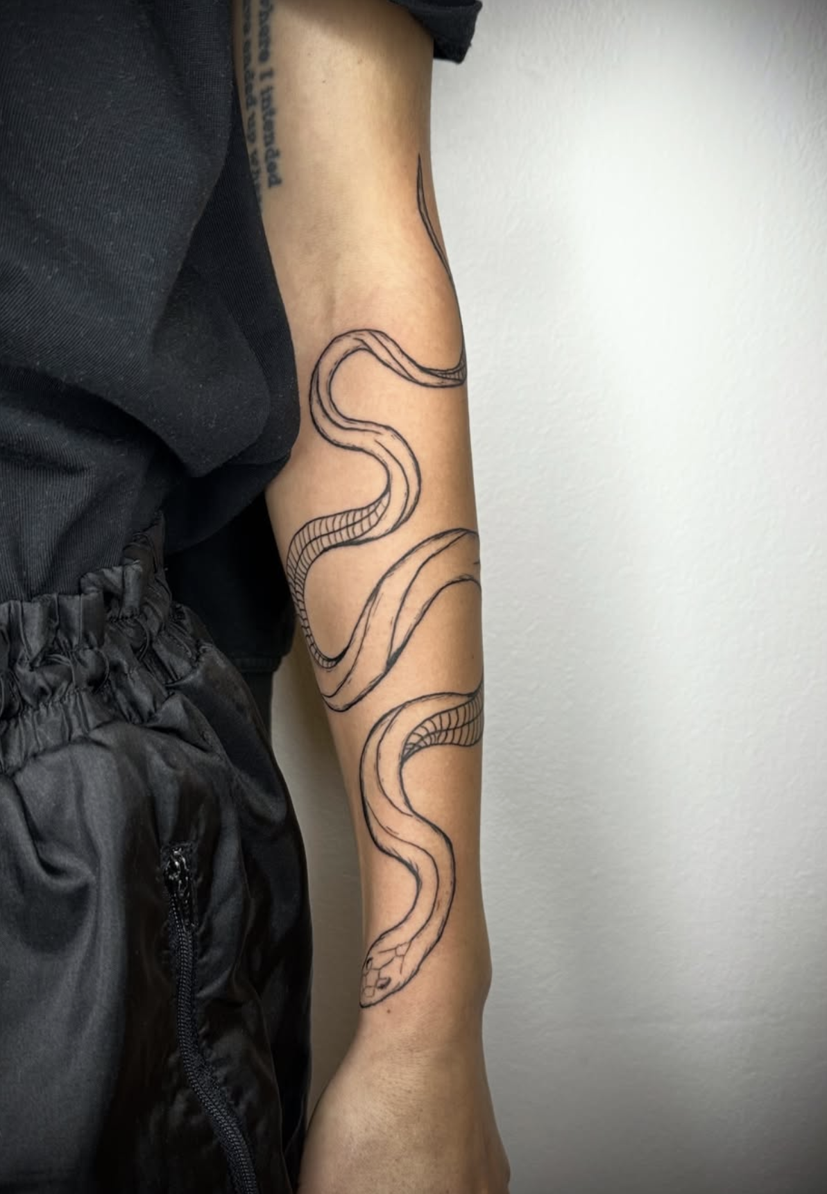 Linienzeichnung eines Schlangenmotivs auf dem Arm einer Person.
