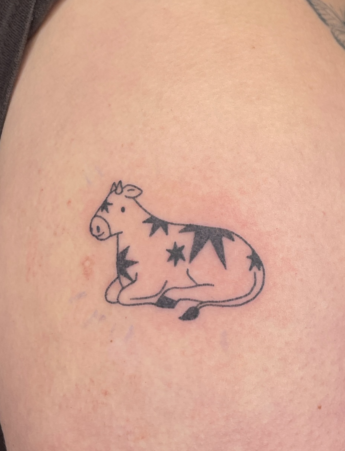 Tattoo einer sitzenden Ziege mit schwarzen Stern- und Streifenmustern auf dem Fell.