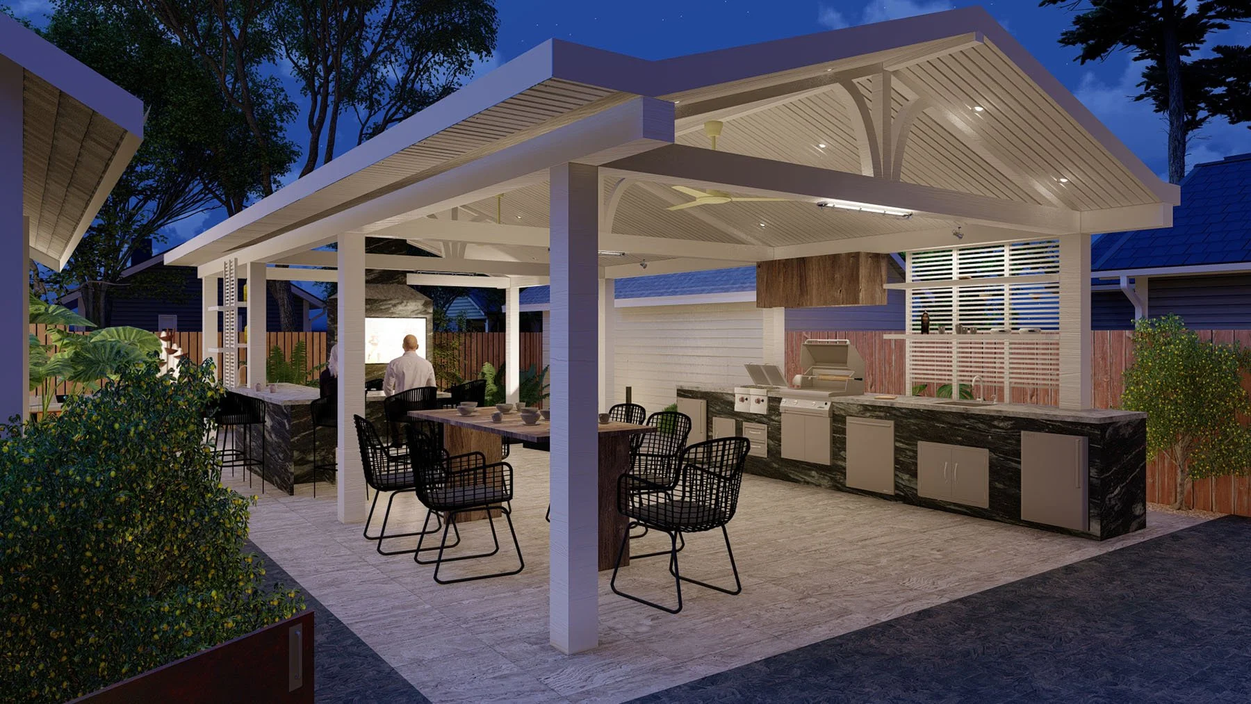 Nighttime outdoor living area with built-in kitchen, bar seating, and a projector screen, surrounded by wooden fencing and trees.
