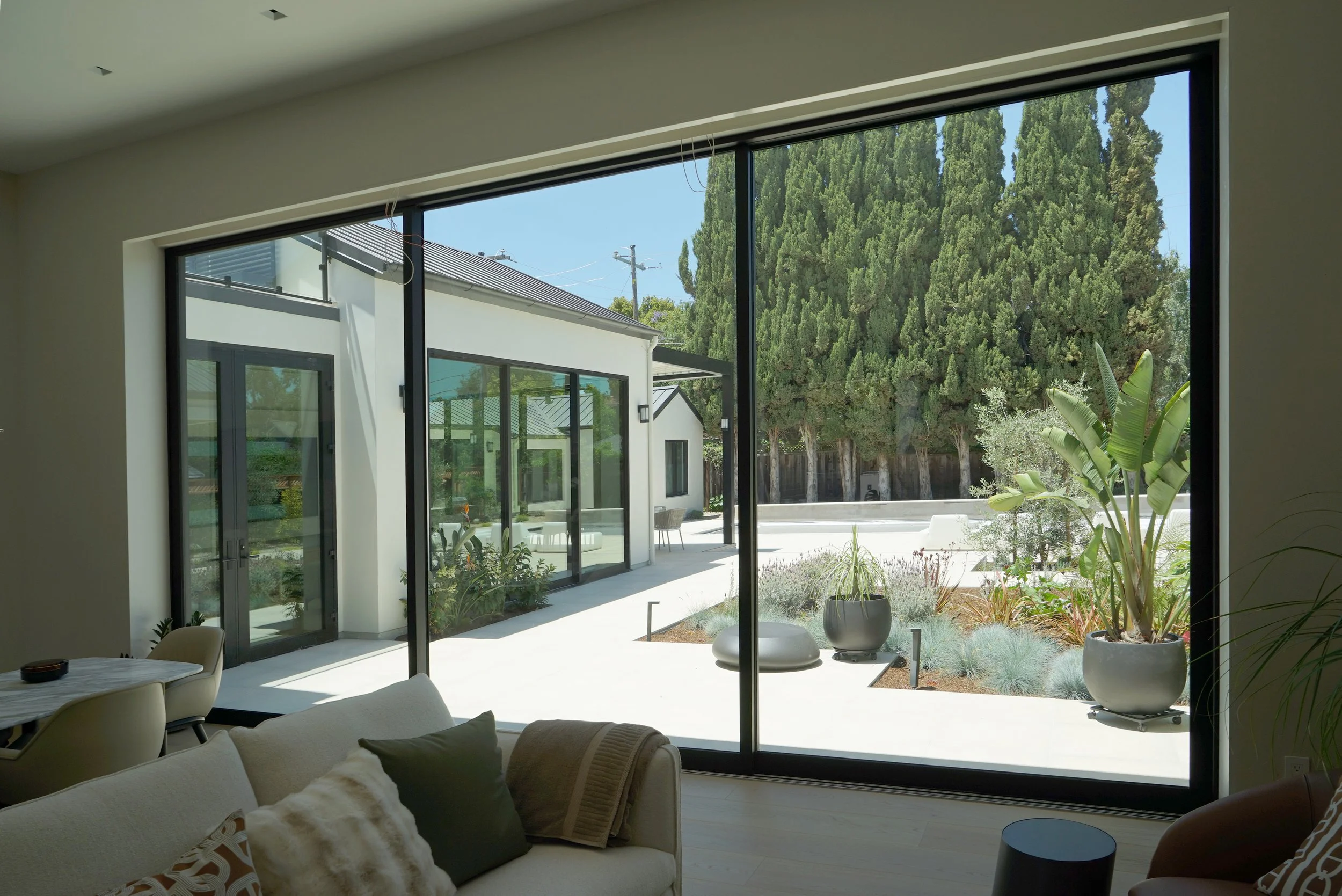 Living room with large floor-to-ceiling glass sliding doors leading to a modern outdoor patio with potted plants and trees.
