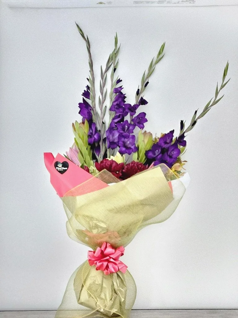 Bouquet with purple flowers wrapped in gold tissue with pink accents and bow.