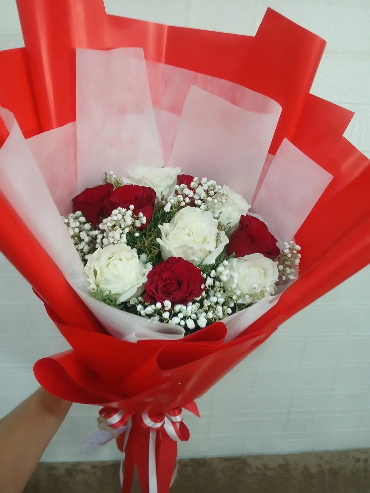 Bouquet of red and white roses with baby's breath, wrapped in red and white paper.