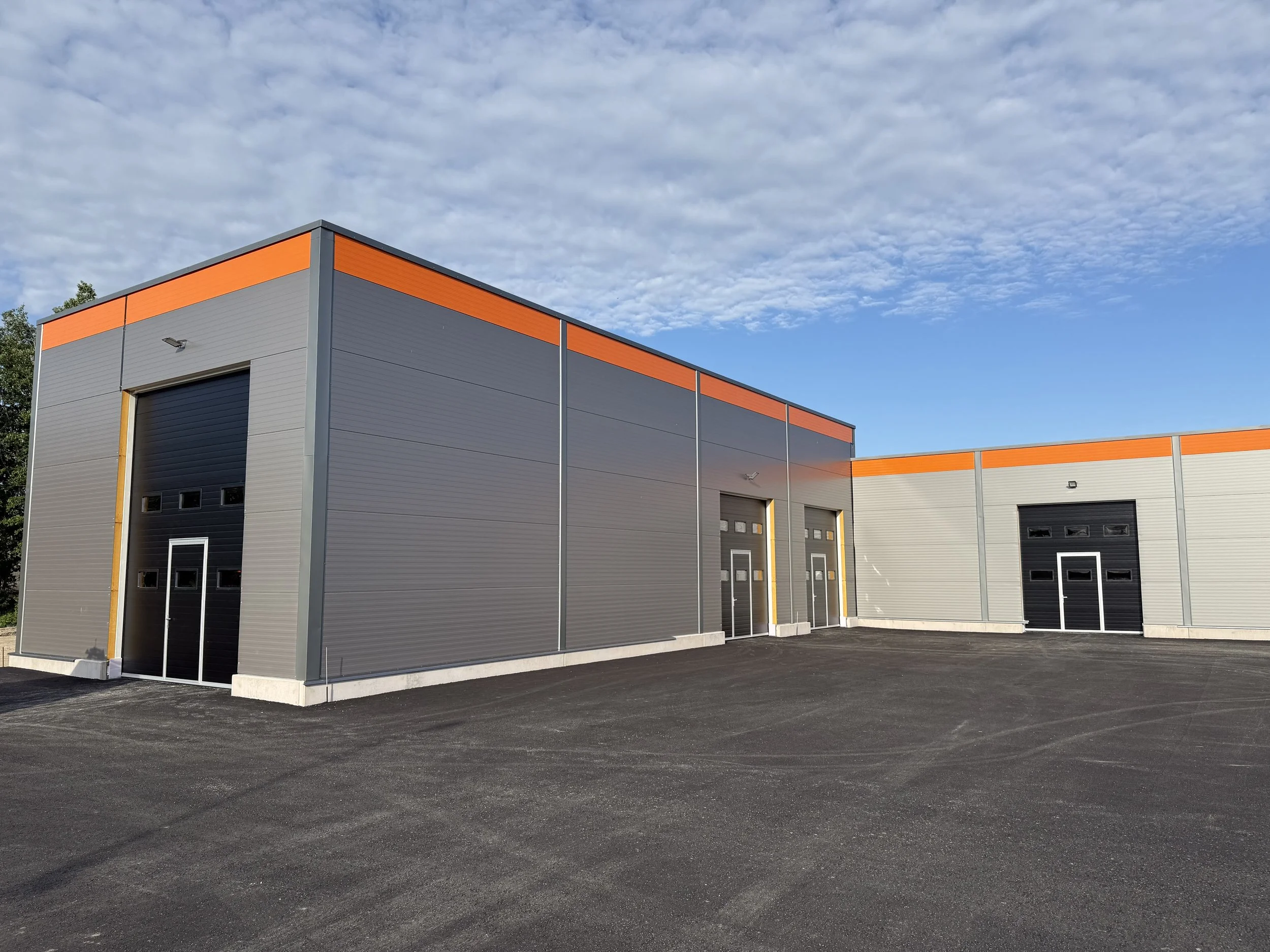 Three gray industrial garage doors with small windows, set in a beige metal building.