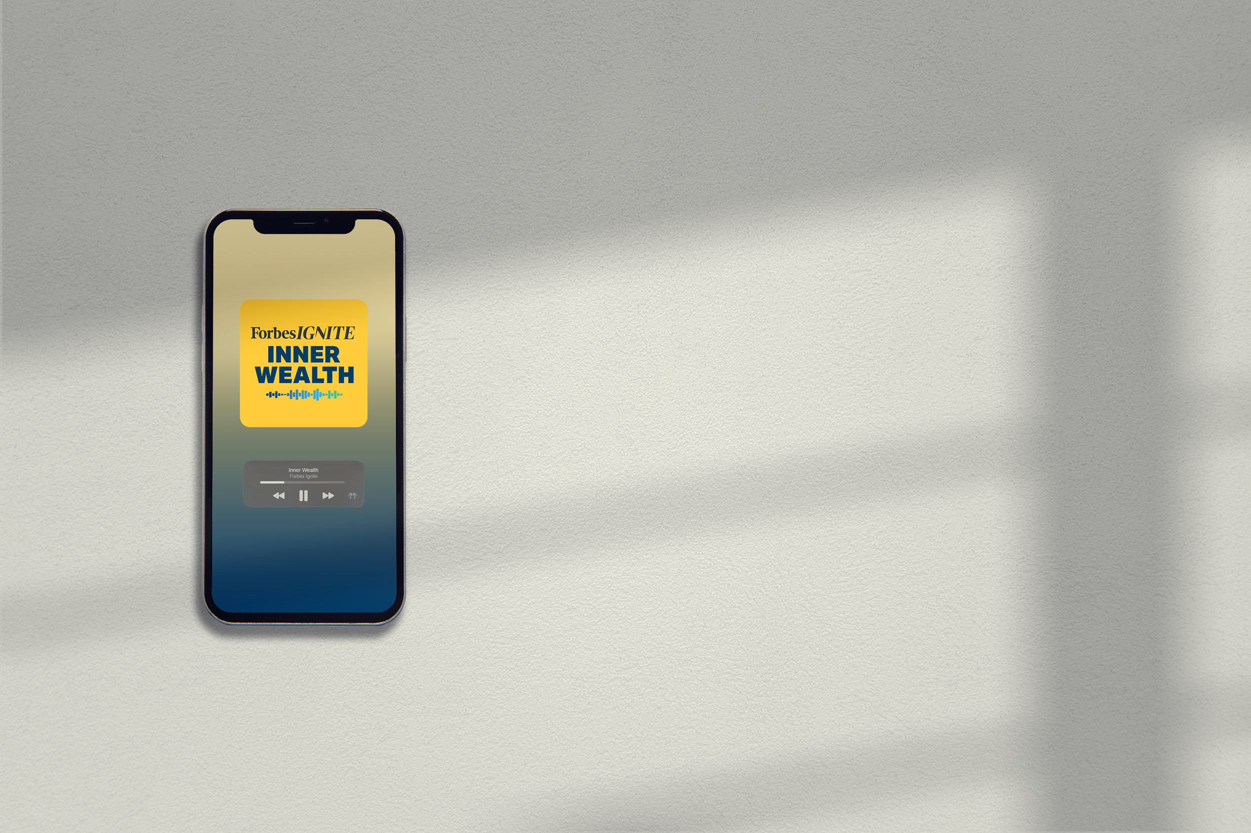 Smartphone displaying a podcast episode titled 'Inner Wealth' on Forbes Ignite, resting on a textured, light-colored surface with shadows.