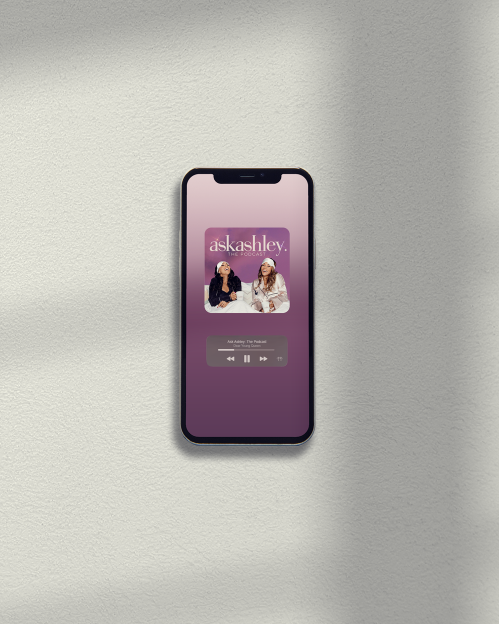 An iPhone displaying the podcast 'Ask Ashley' on a white surface