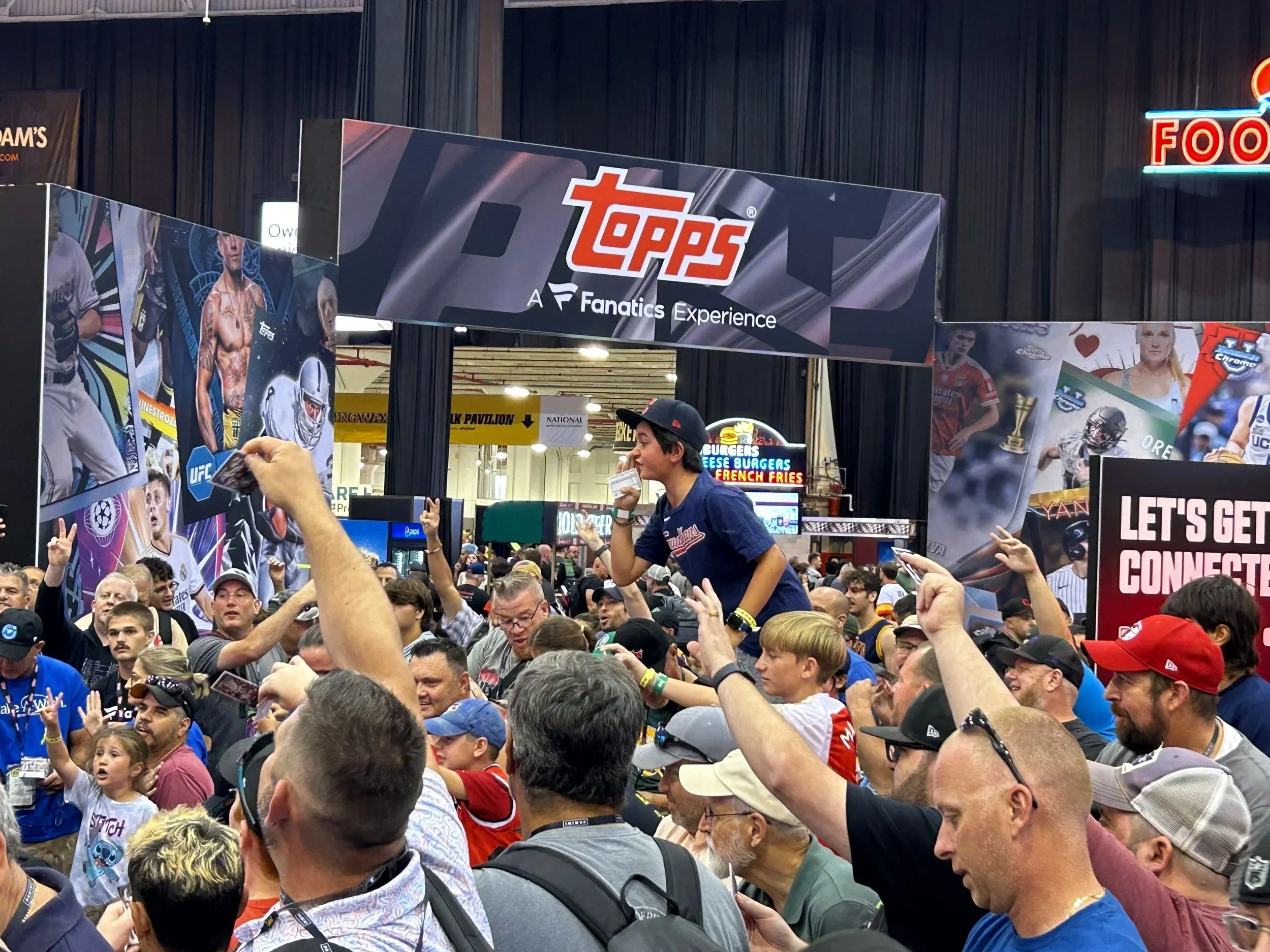 Crowd of people attending a sports card trading event at the Topps Fanatics Experience booth, with some fans getting ready for pack wars.