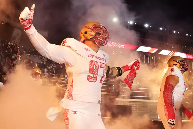 A football player in a white and red uniform with the number 22, wearing a yellow helmet, raising his right arm as smoke surrounds him during a game at night.