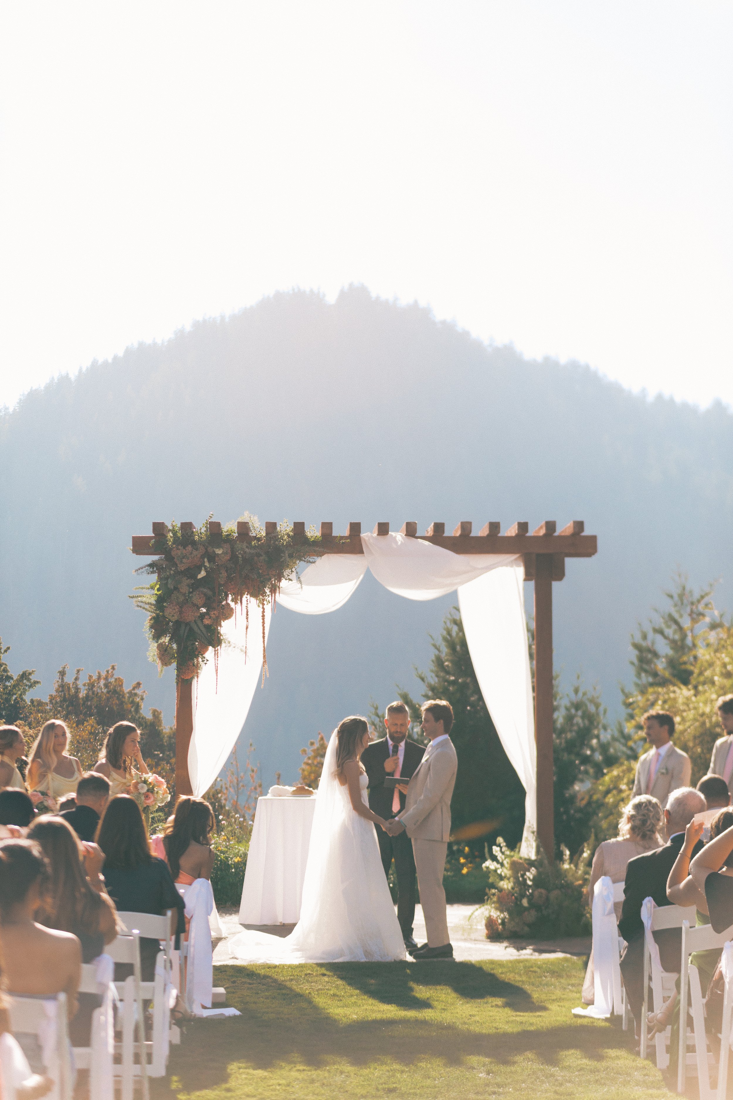 bride and groom in front of asymmetrical floral arbor with mountains.