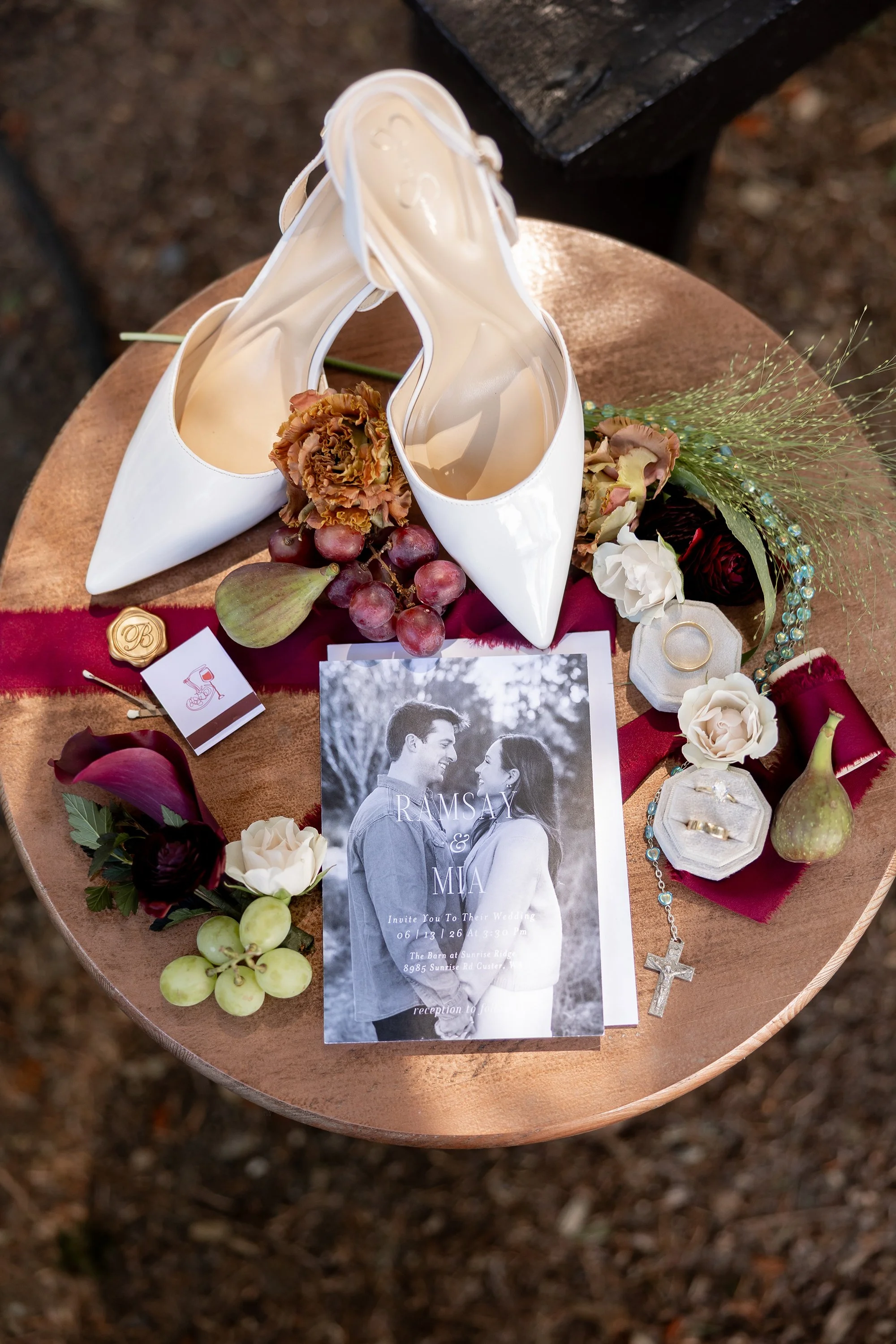 A flatlay with the bride's heels, fruit, rings, grapes, a matchbook and the wedding invitation showing the happy couple.
