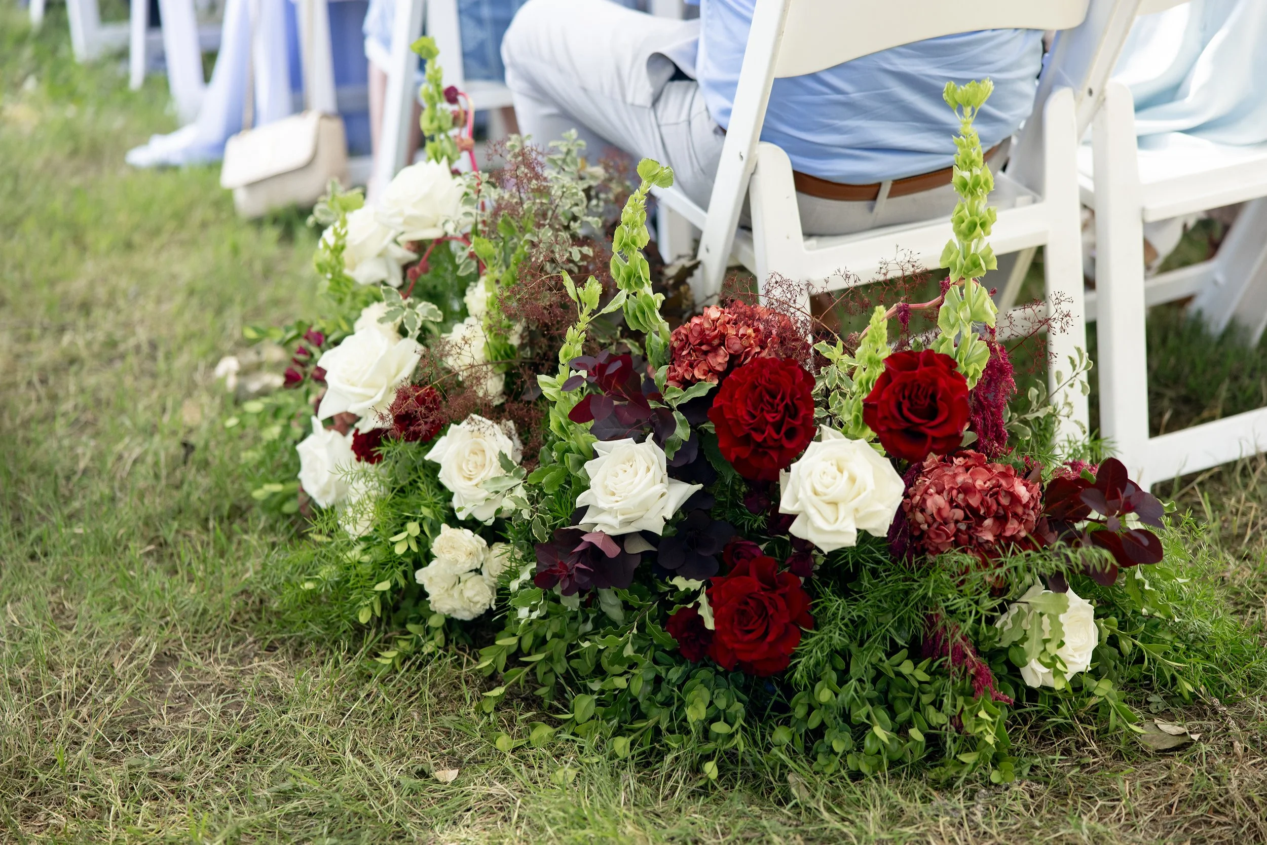 aisle arrangement for wedding featuring wine colored blooms, white roses and boxwood.
