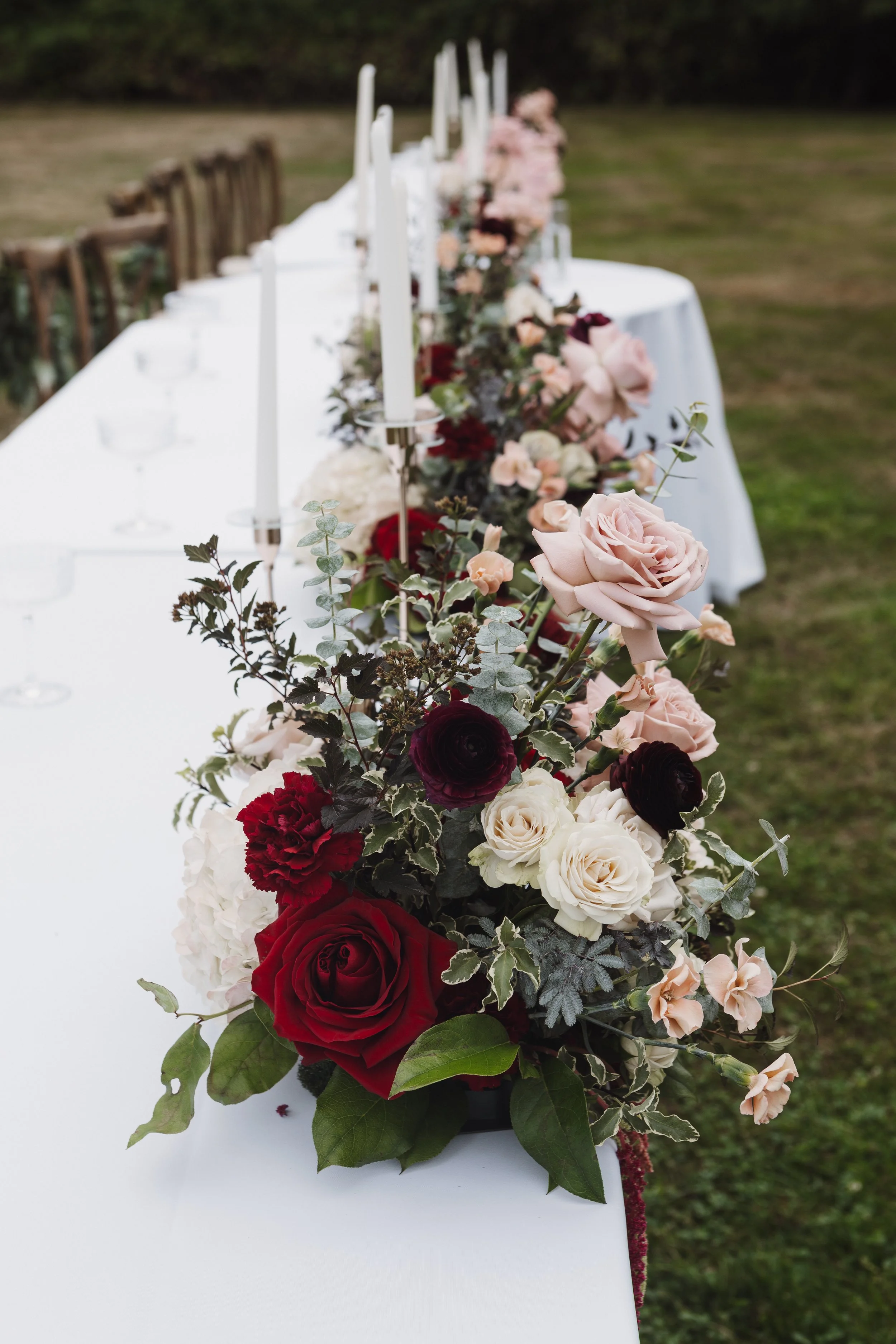 wedding reception table runner with blush, mauve and burgundy flowers and candles.