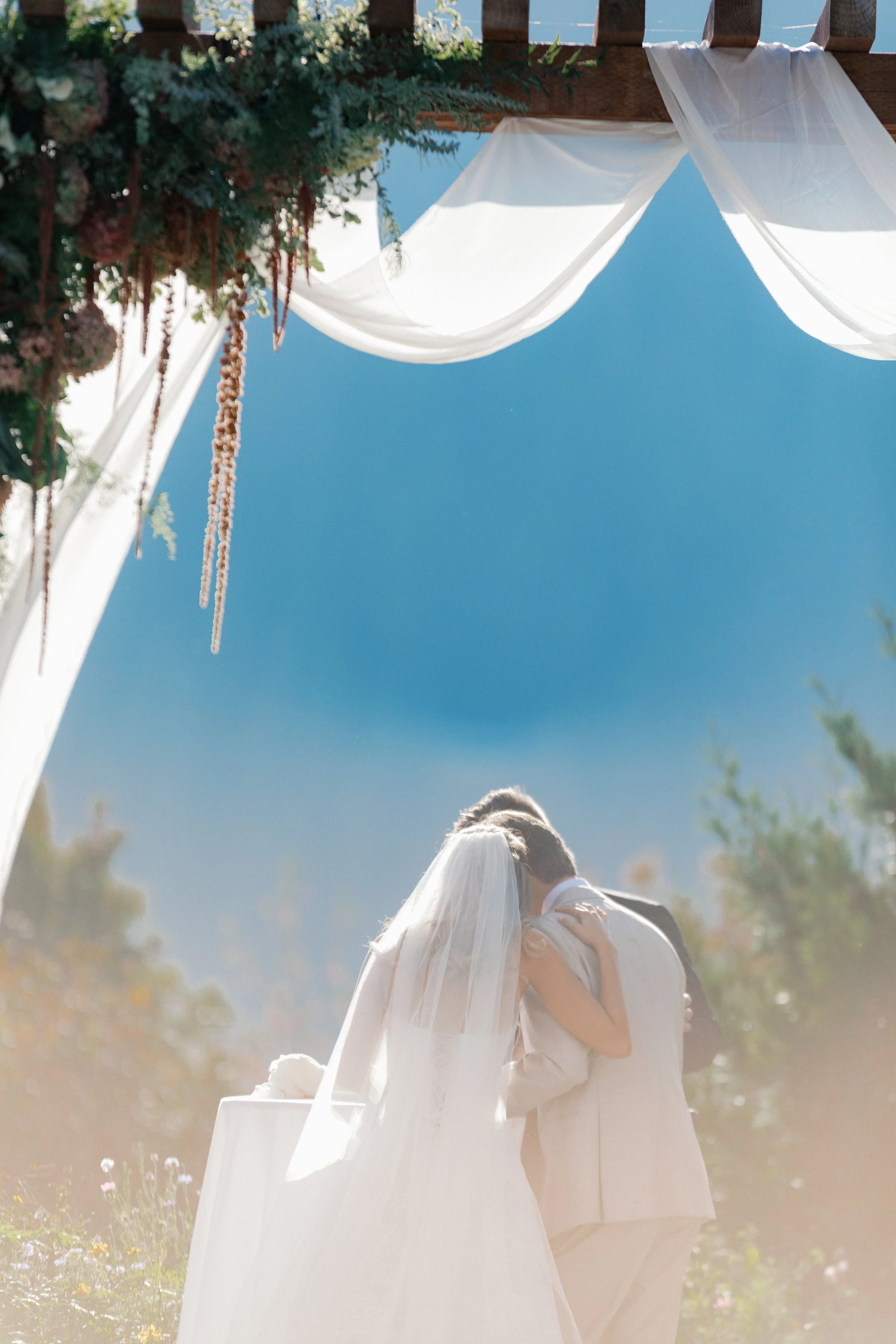 bride and groom under an asymmetrical floral arbor in front of mountains.
