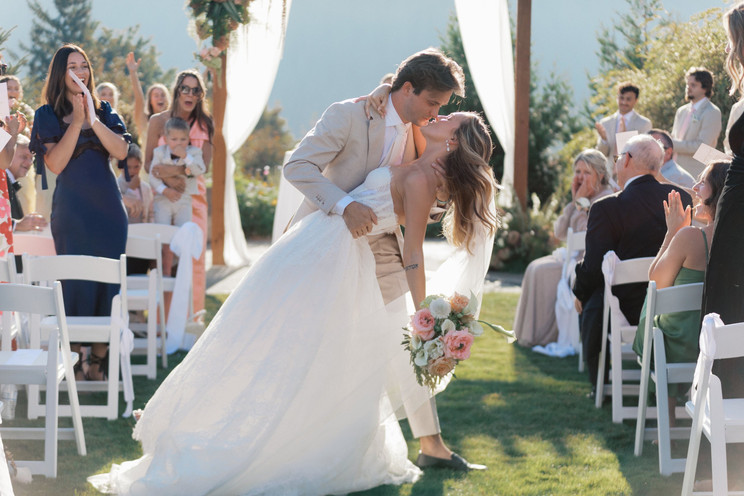 Bride and groom kissing in front of an asymmetrical floral arbor.