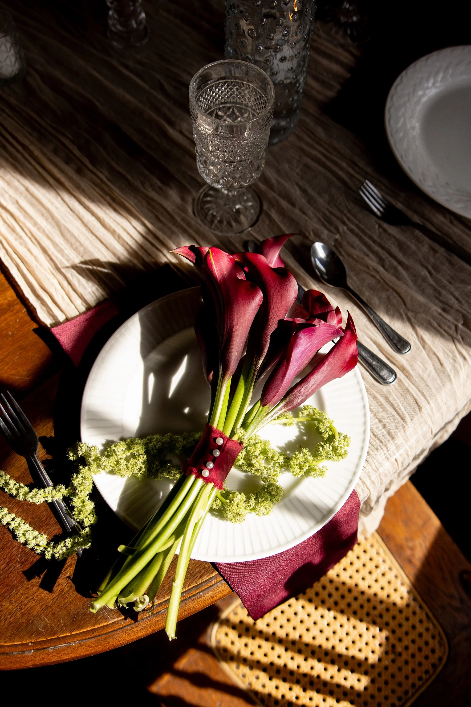 wine colored calla lillies and lime amaranth in a bouquet on top of a simple place setting.