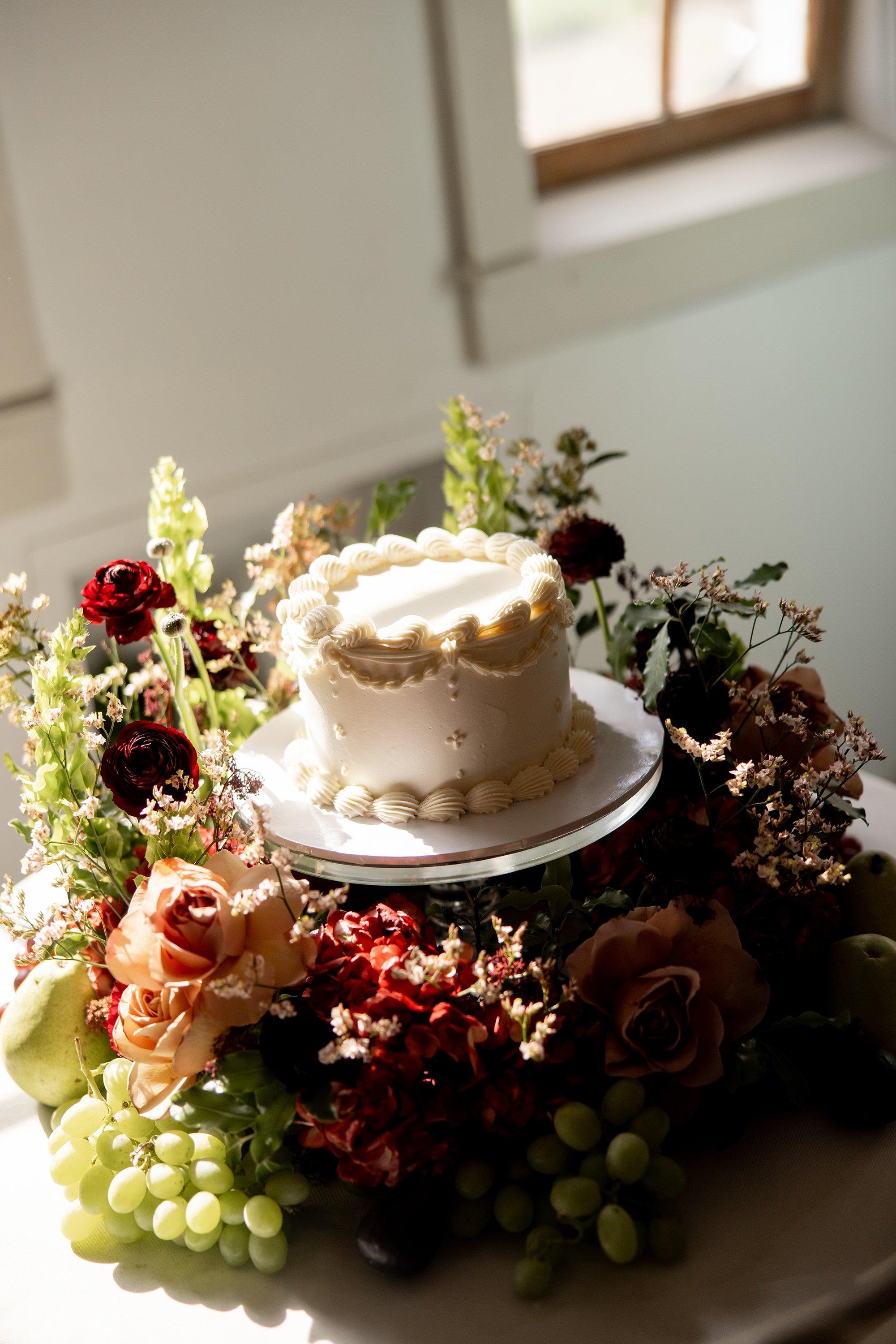 simple cake surrounded by abundant wine, mauve and green florals and fruit