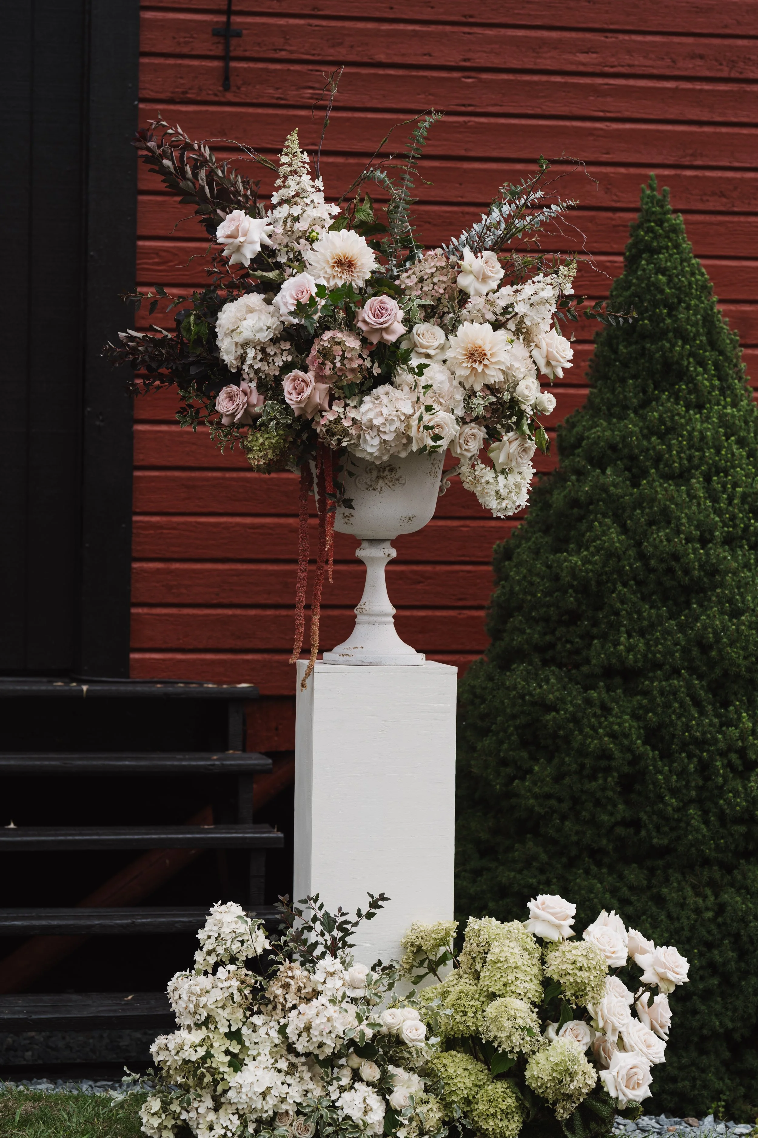 A dramatic draping floral urn arrangement on a column, surrounded by a ground meadow.