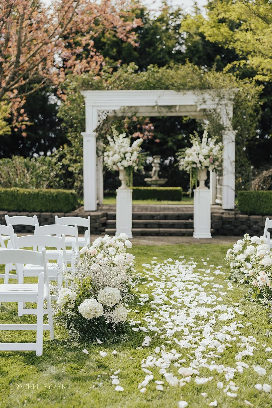 Ceremony area with ombre petal path, ground meadow lining aisle, and tall arrangements flanking ceremony