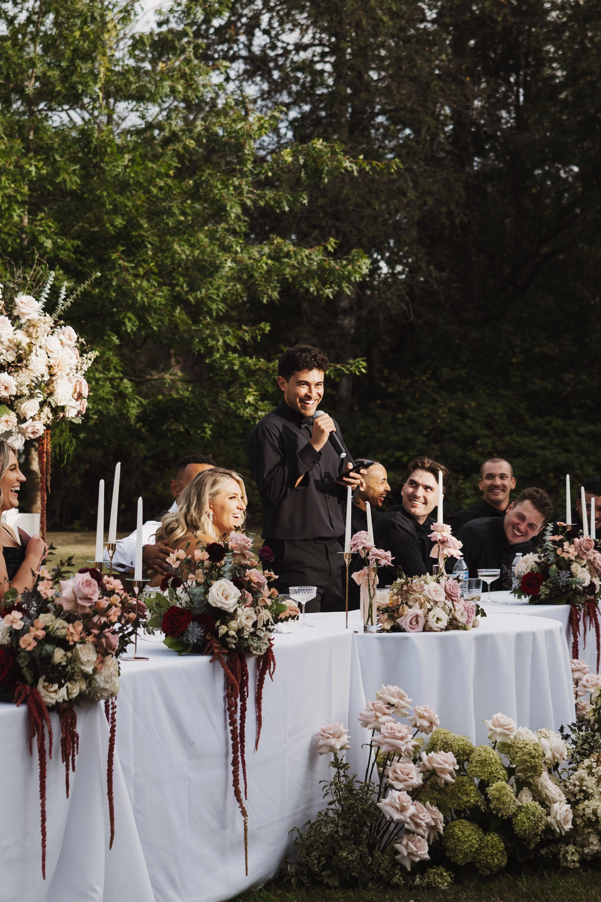 Dramatic florals drape the wedding reception head table. Mauve roses and cream accents mix with draping burgundy amaranthus and pops of green.