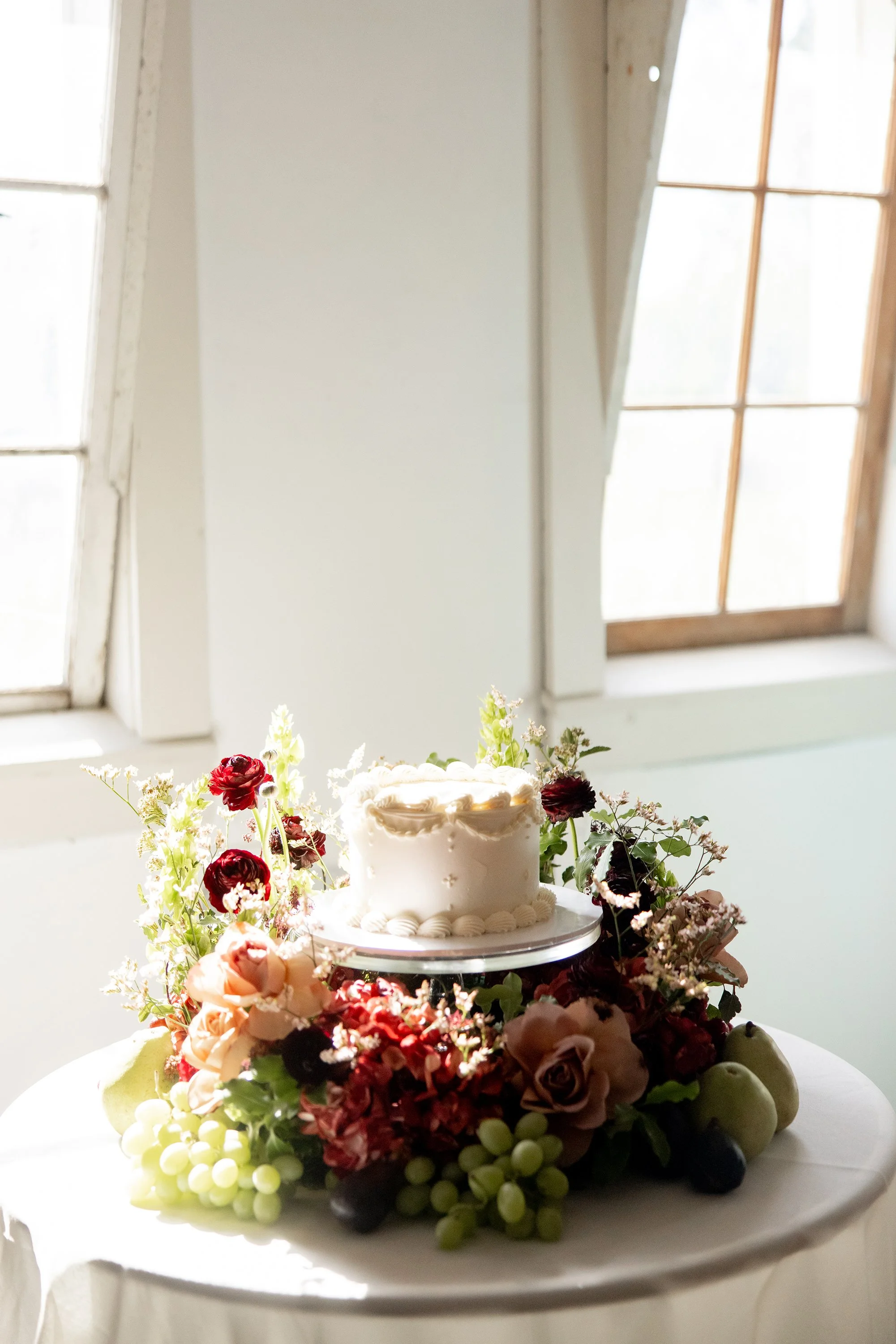 simple white wedding cake surrounded by cake meadow florals and fruit