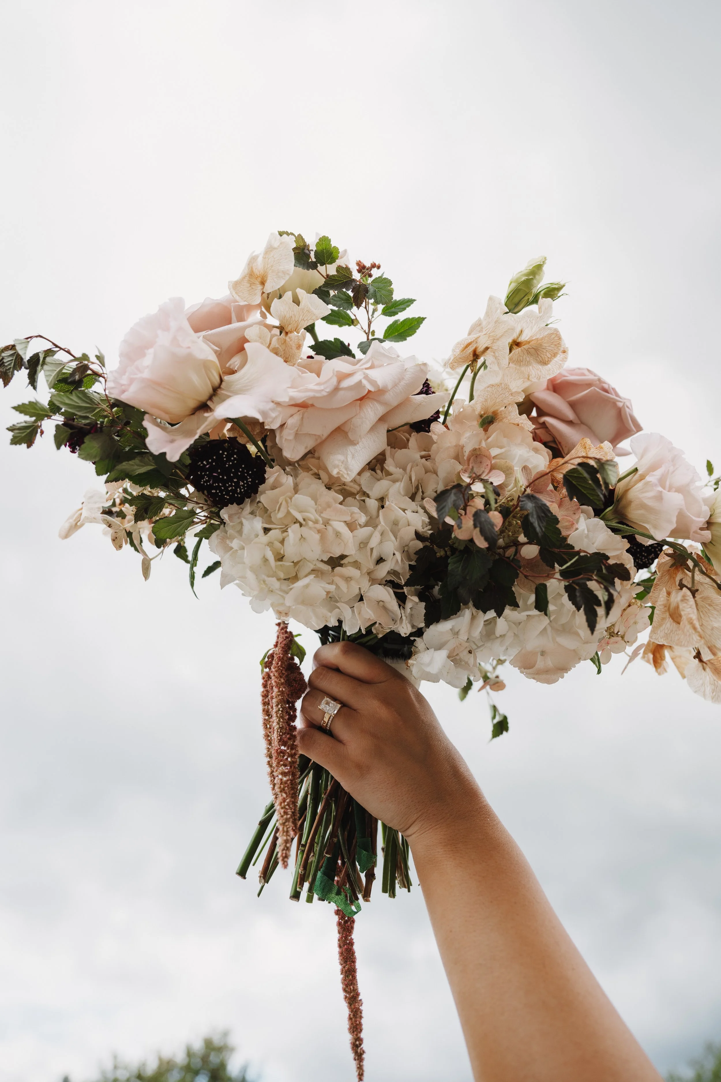 A beutiful bridal bouquet against the sky, with cream, mauve, blush and burgundy florals.