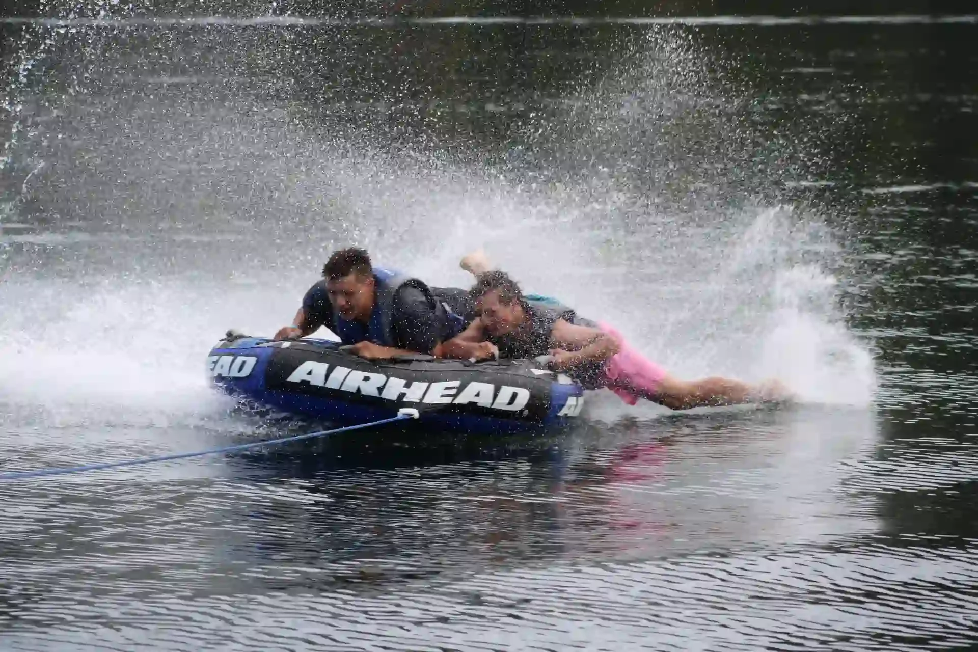 Two young men tubing, water spraying behind them